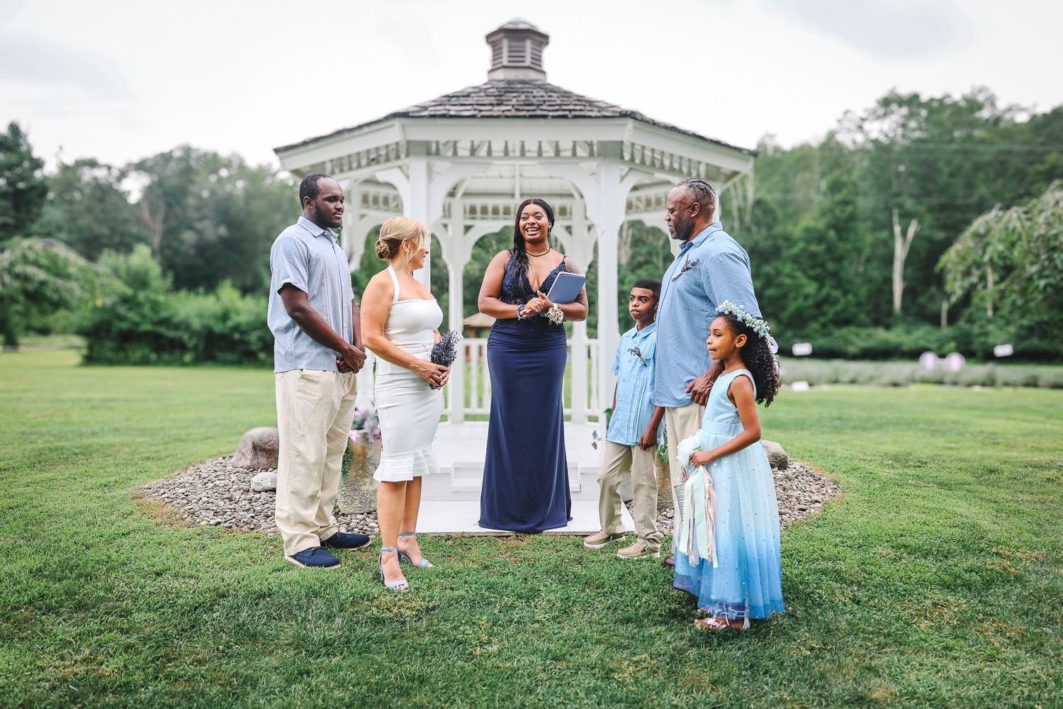 A group of people gather outdoors on a grassy lawn for a summer celebration event.