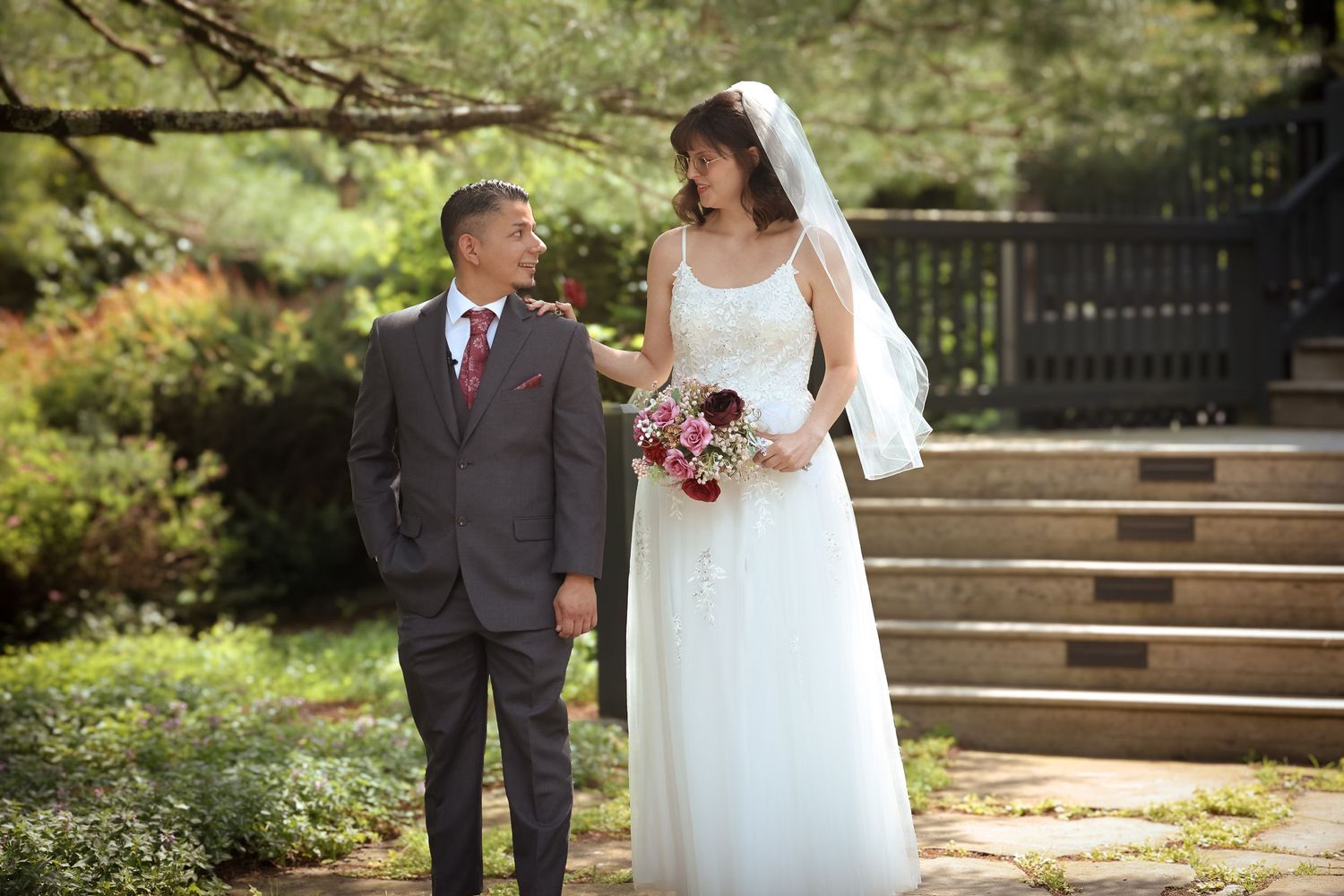 A couple in wedding attire walks together in a lush garden setting during their outdoor ceremony.