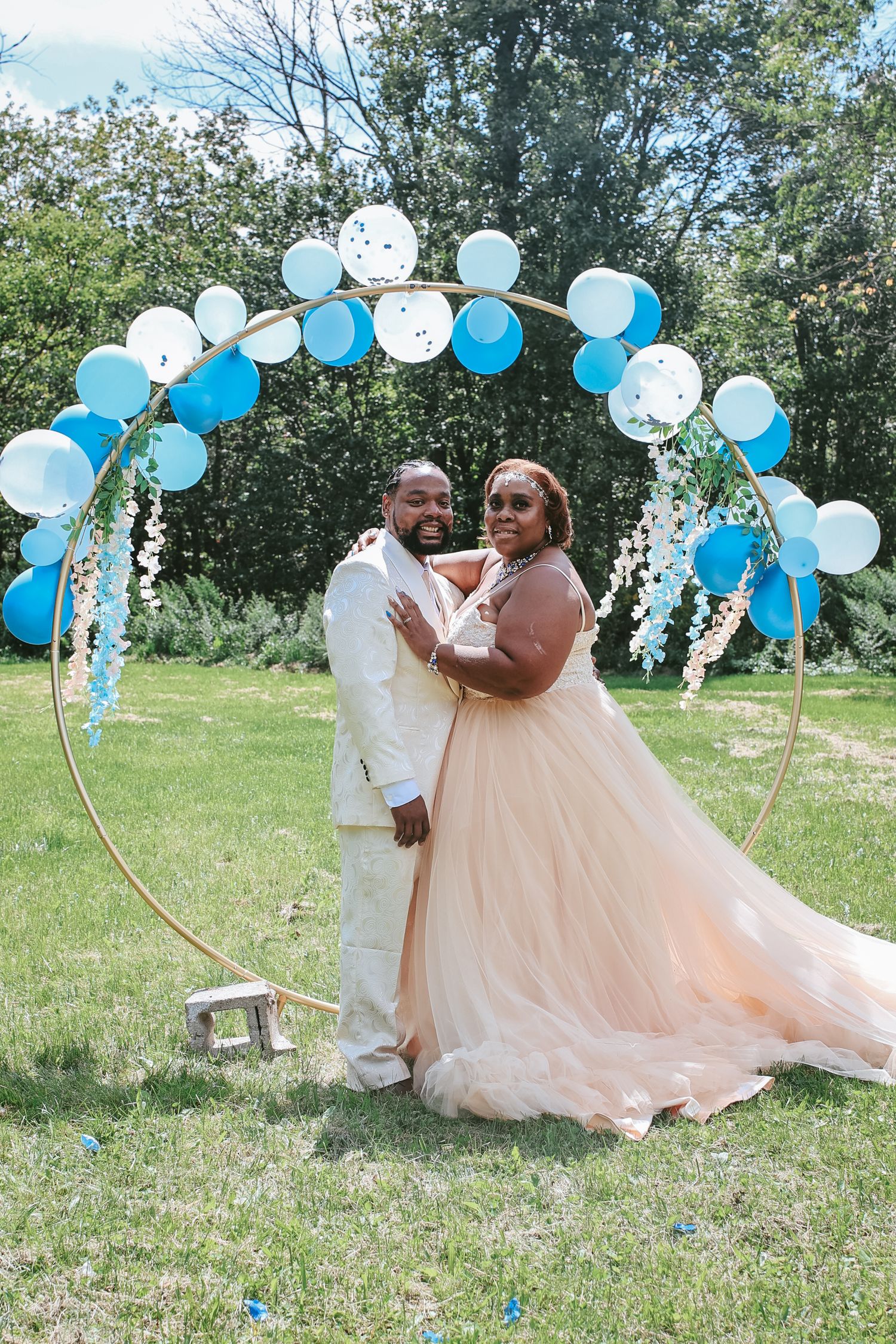 A romantic outdoor celebration with blue and white balloon arches decorating a sunny field where a couple shares tender moments.