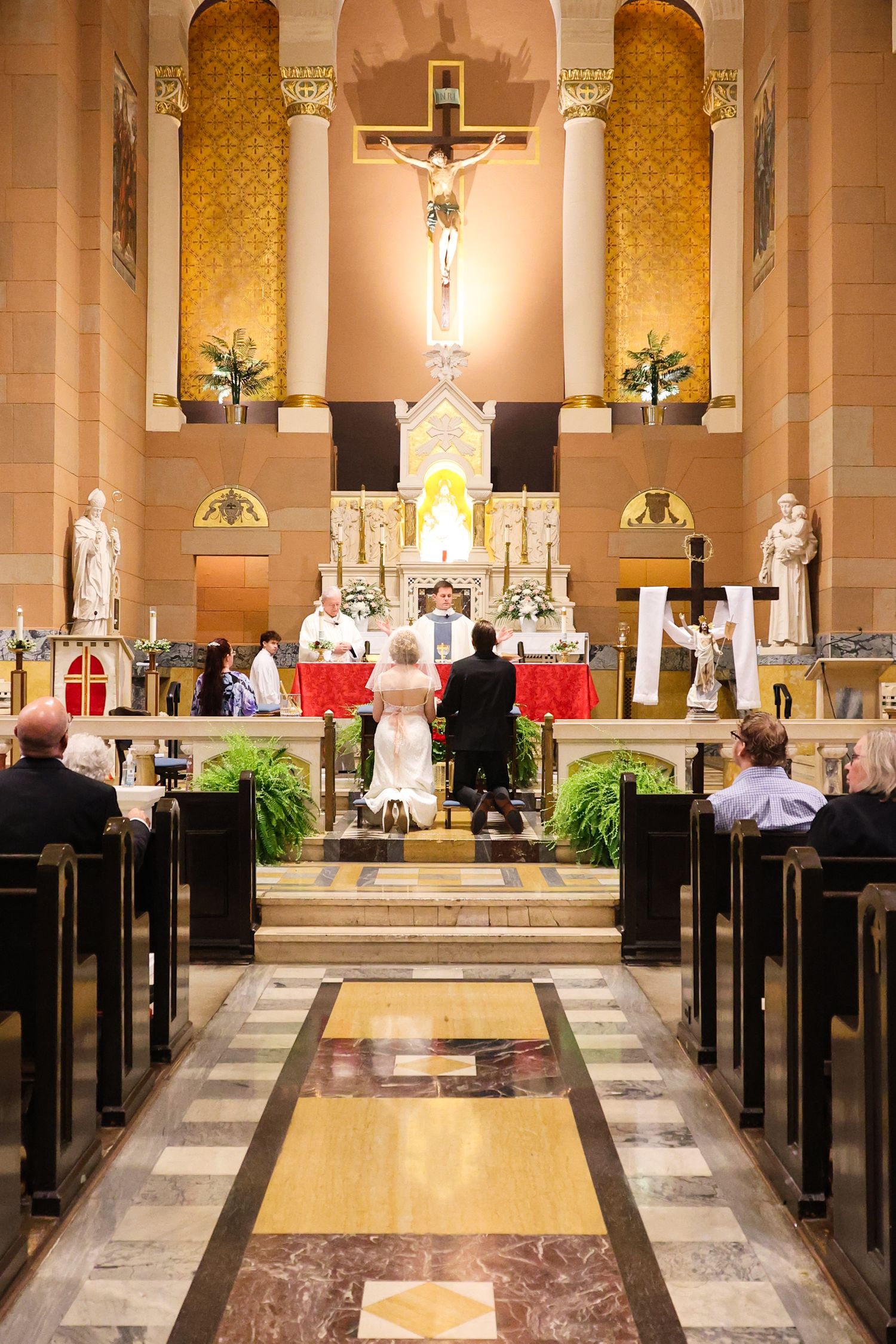 Interior view of a Catholic church during a mass ceremony with ornate columns and altar decorated with flowers and candles.
