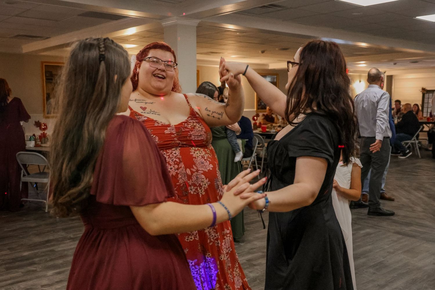 People dancing together in a dimly lit indoor venue with hardwood floors and overhead lighting.