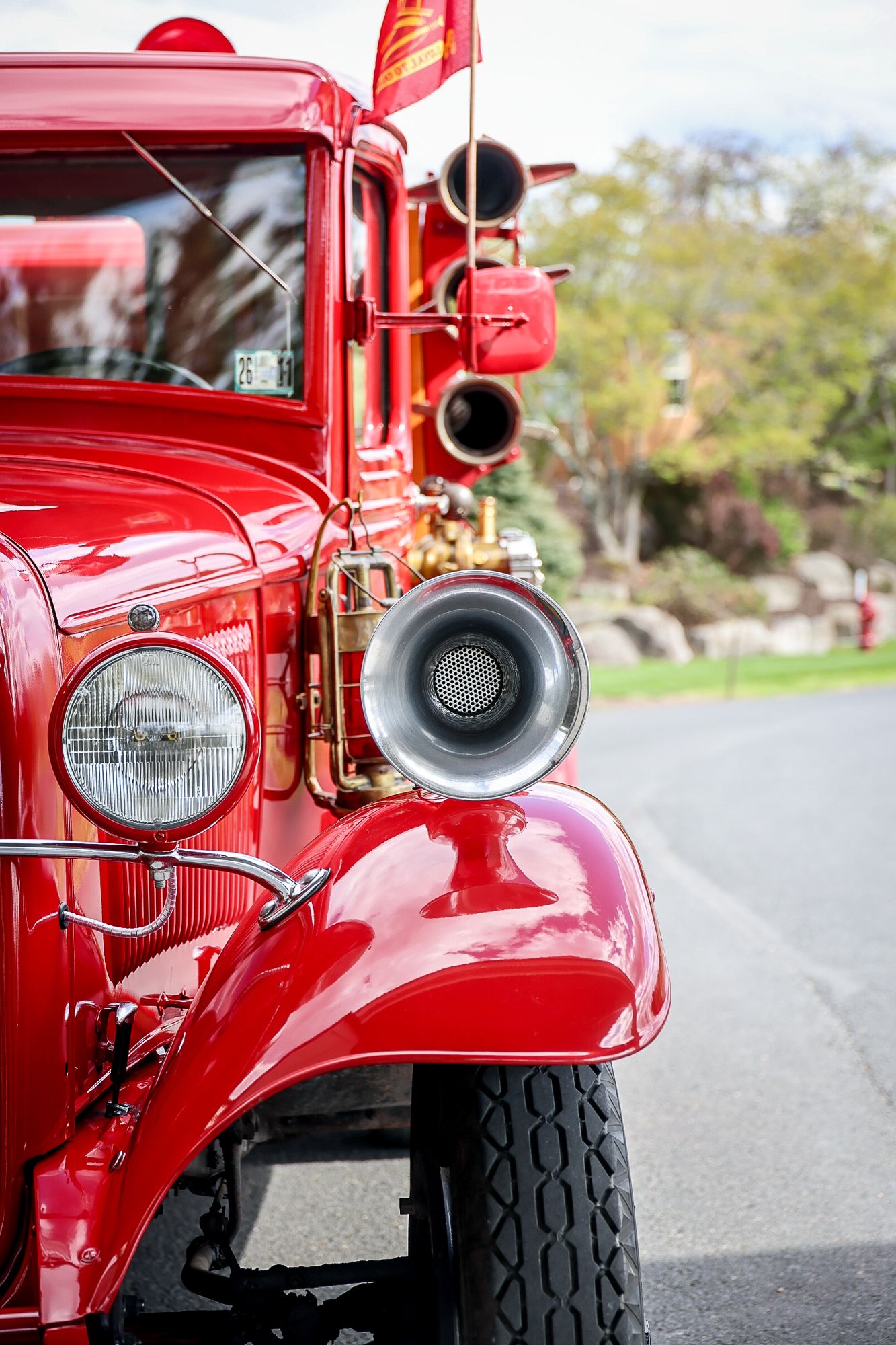 Vintage red fire truck front view showcasing chrome horn, headlight, and polished fender parked on a suburban street.