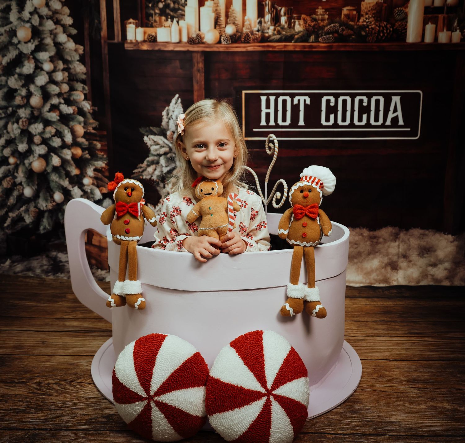 Girl sitting in giant mug prop with gingerbread dolls at a festive hot cocoa Christmas photo session.