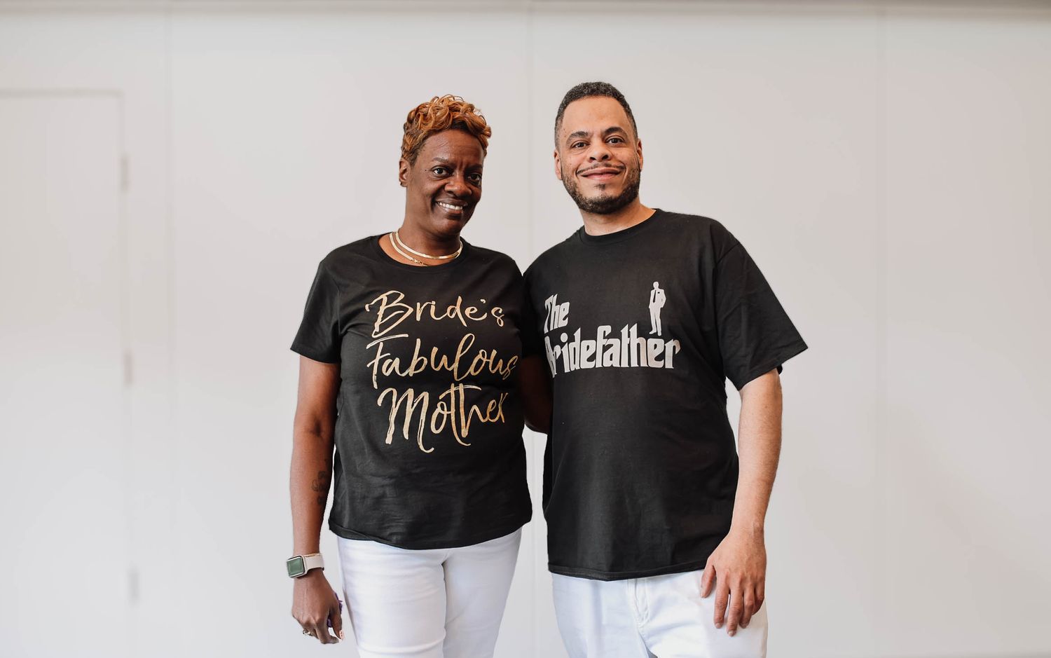 Bride's mother and groom wear matching black shirts with wedding-themed text at a wedding celebration.
