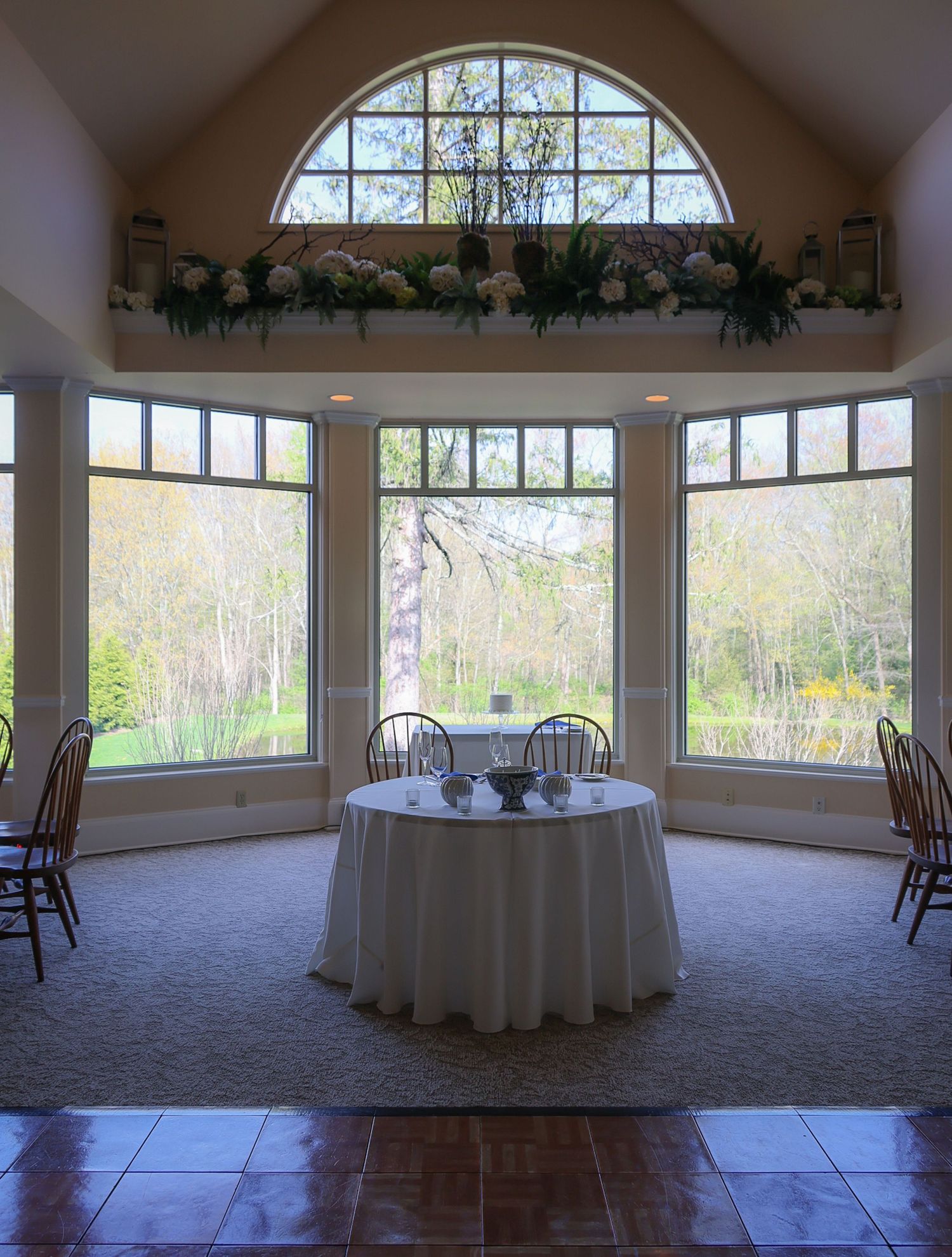 Elegant sunroom with round table, floral arch window, and panoramic garden views, ideal for intimate wedding receptions.