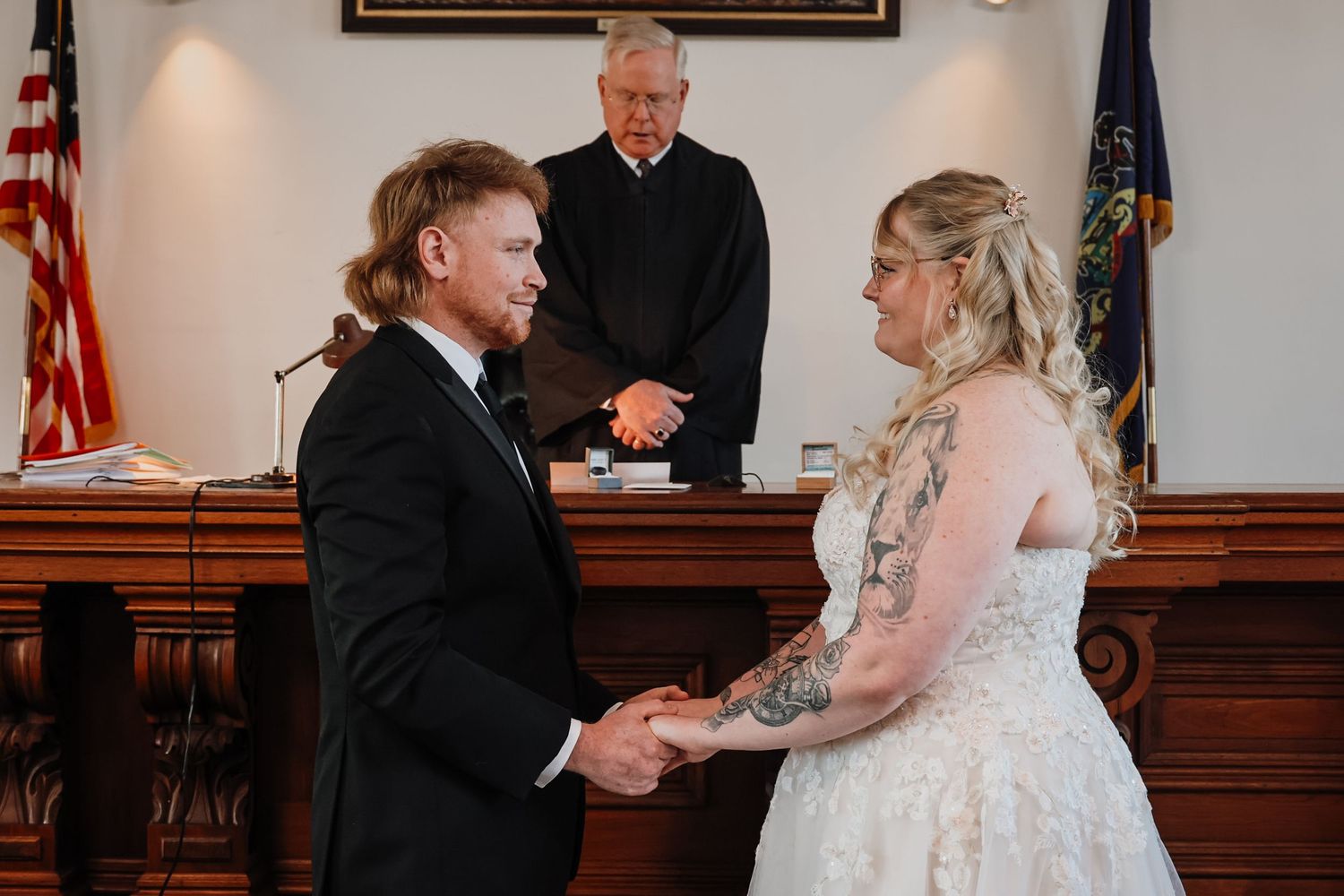 Couple exchanging vows at a courthouse wedding ceremony with a judge officiating, bride in white gown, groom in black suit.