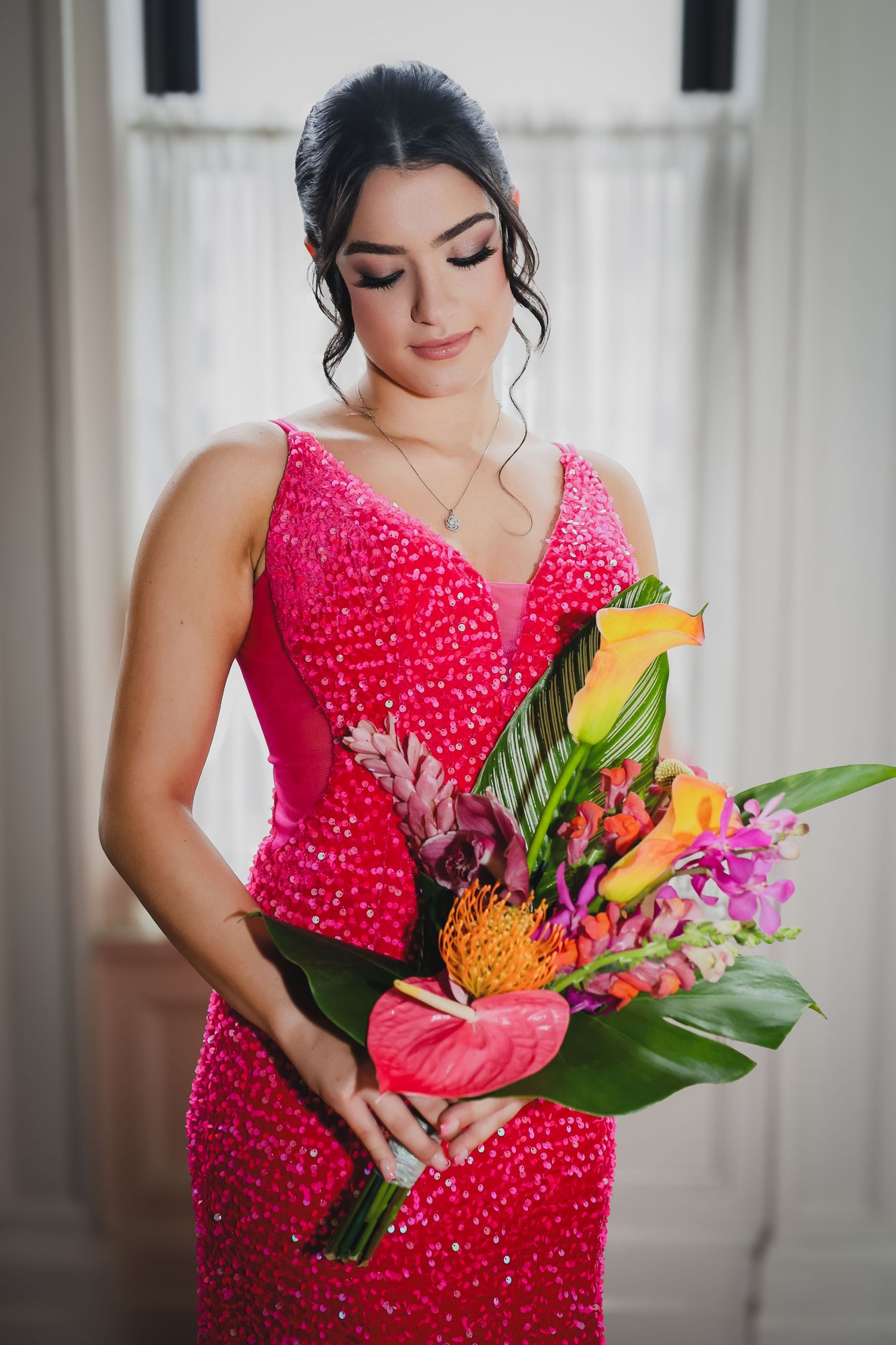 Woman in pink sequin gown holding tropical floral bouquet with anthuriums and orchids, elegant updo hairstyle.