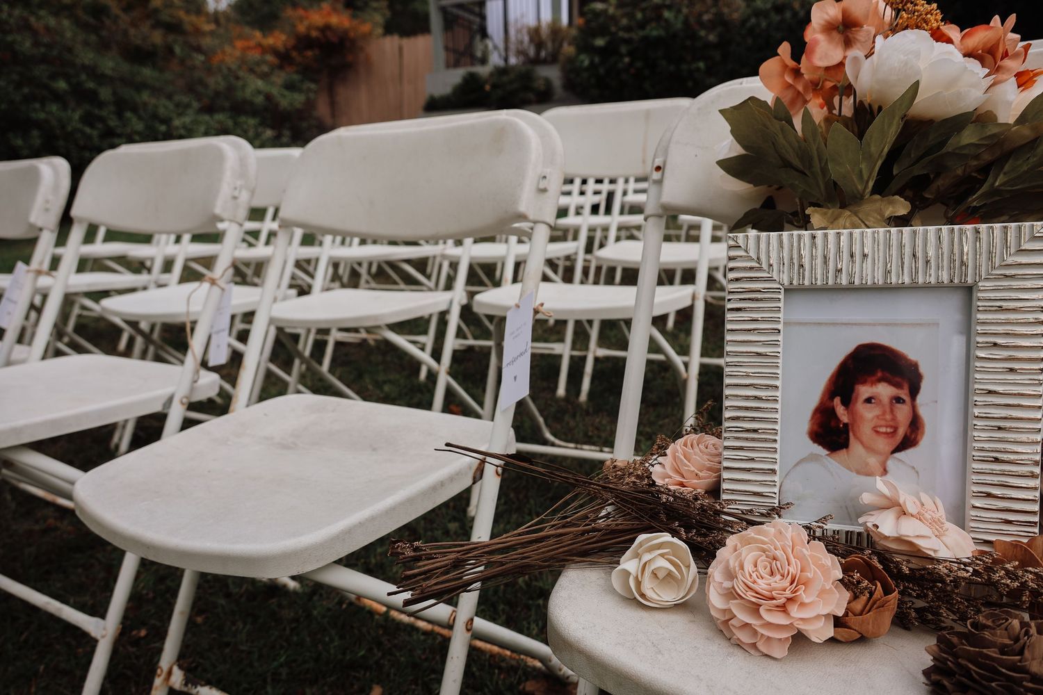 White folding chairs arranged in rows for an outdoor wedding ceremony with pink floral decorations.