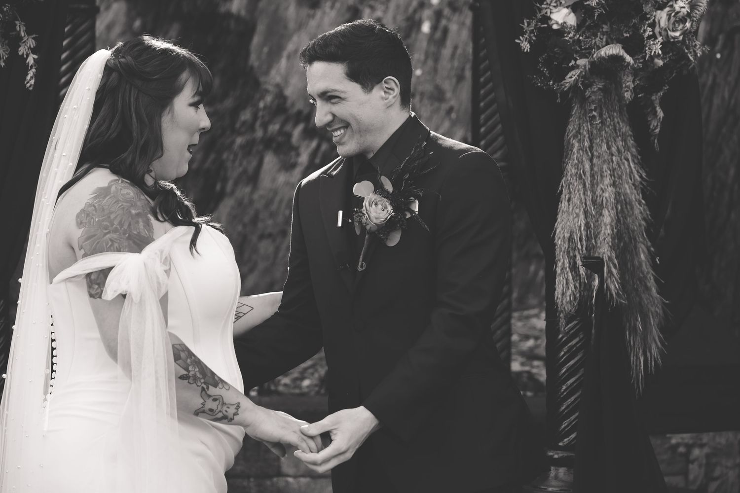 A black and white wedding ceremony photo showing a couple exchanging vows while holding hands at the altar.