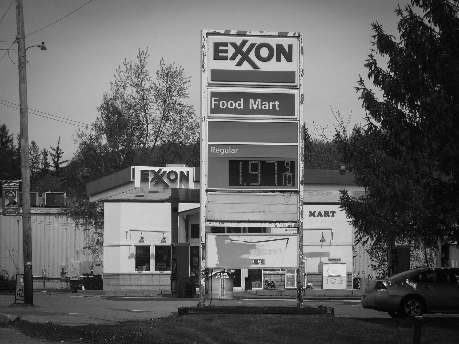 Black and white image of a vintage Exxon Food Mart gas station with tall sign and storefront.