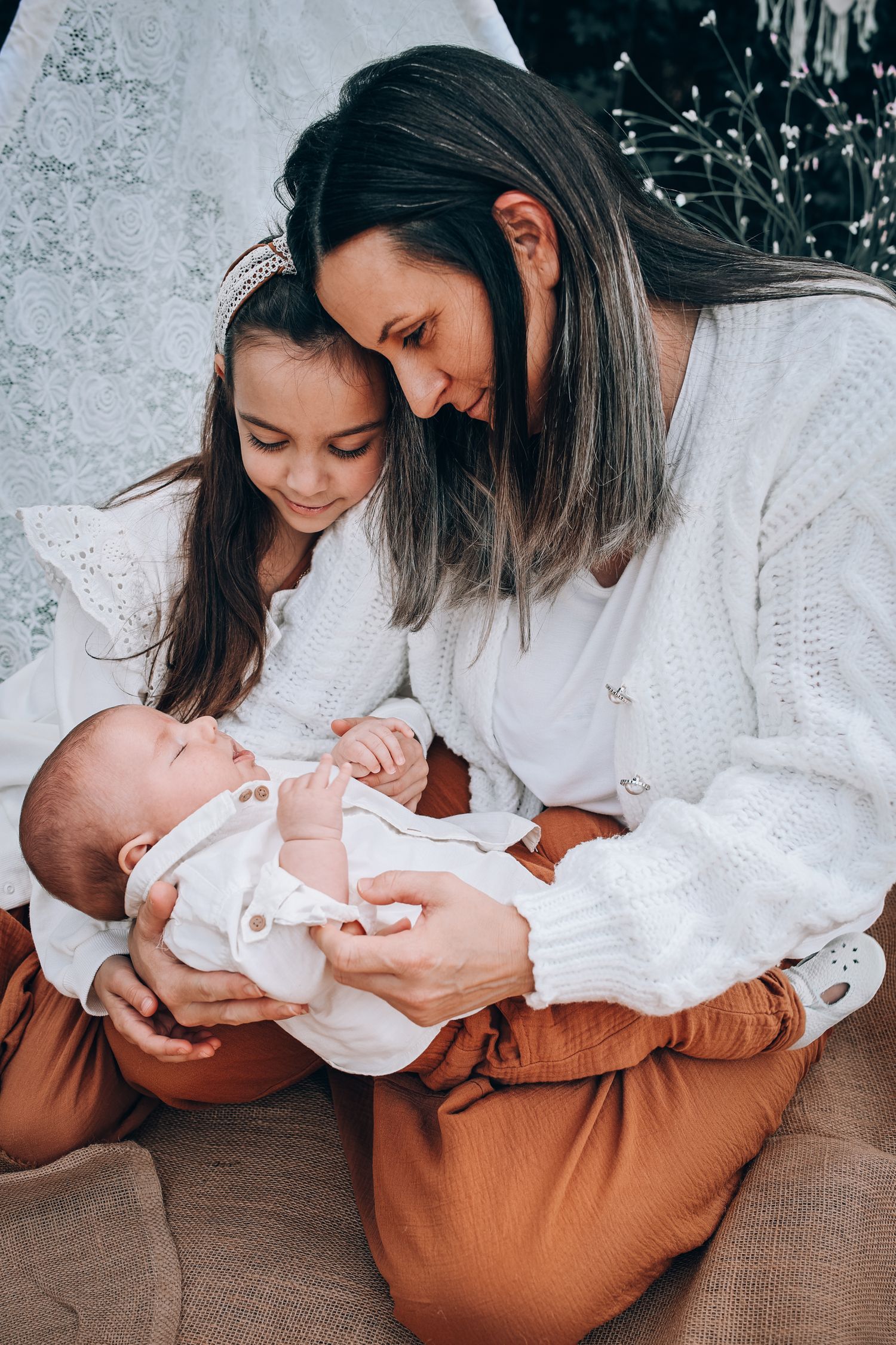 Two people in white sweaters sit together lovingly gazing at a newborn baby wearing white clothing.