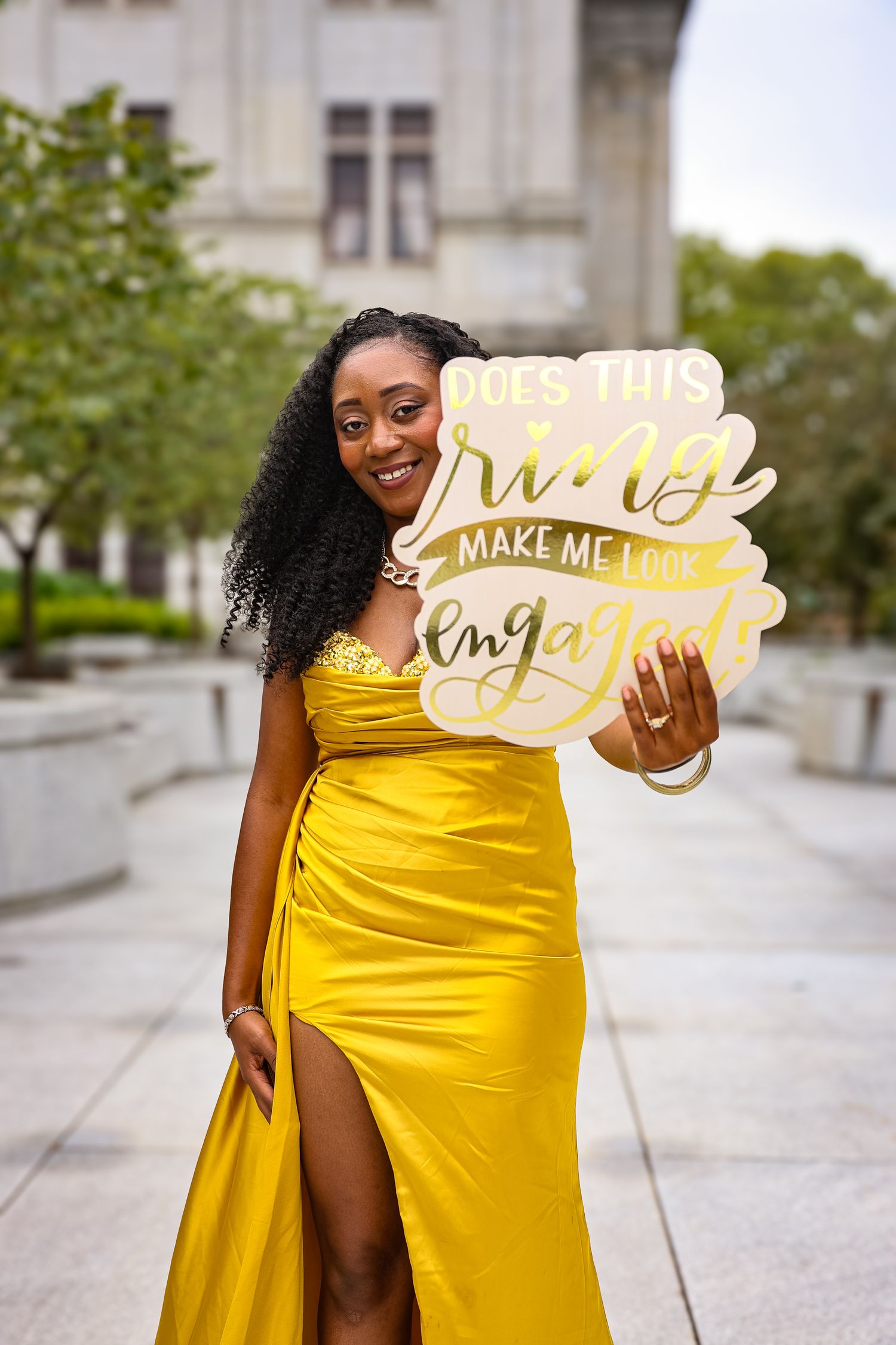 Person in vibrant yellow dress poses with decorative signs on urban sidewalk in creative photoshoot series.