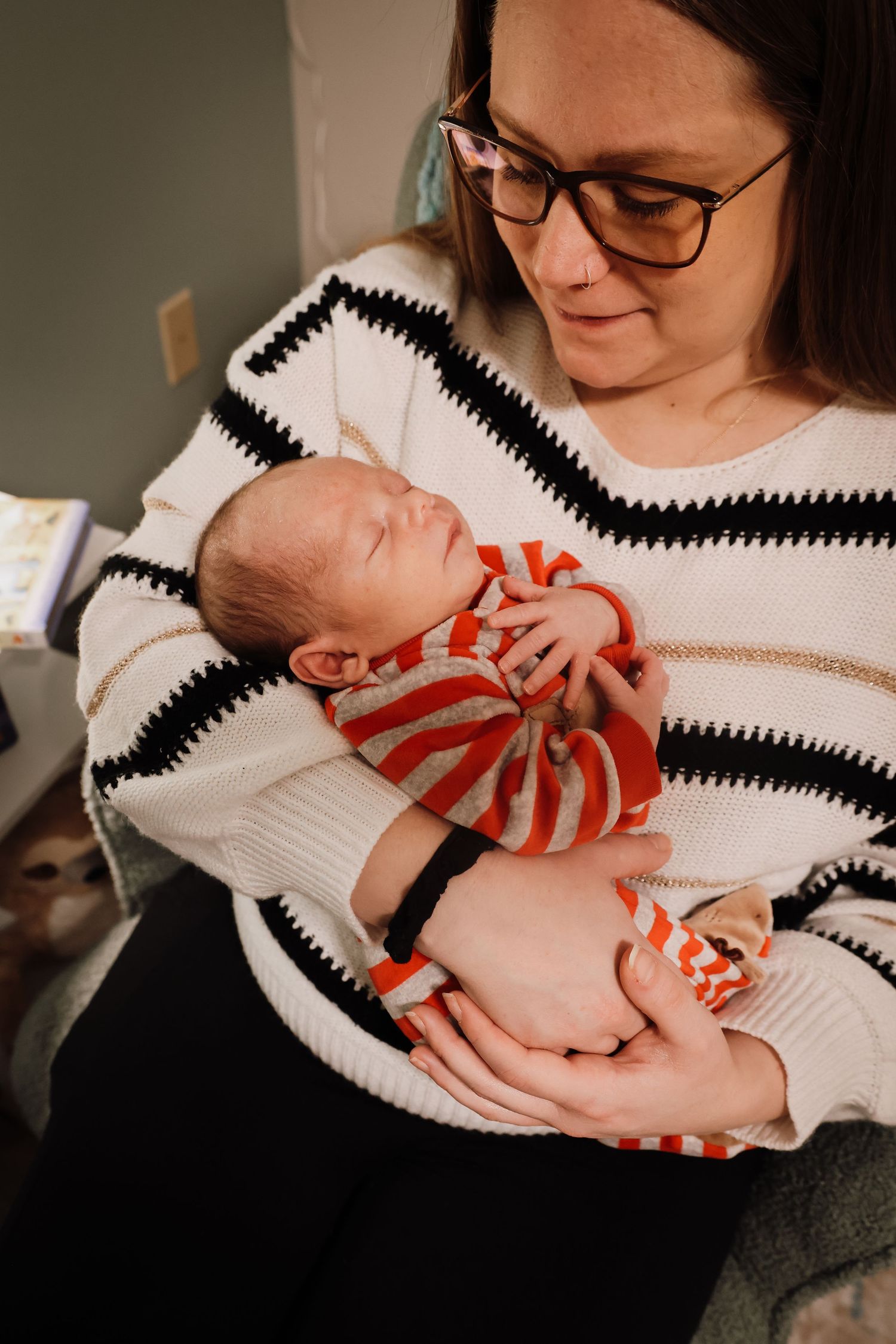 A person wearing glasses and a striped sweater holds and gazes lovingly at a sleeping baby in a series of photos.