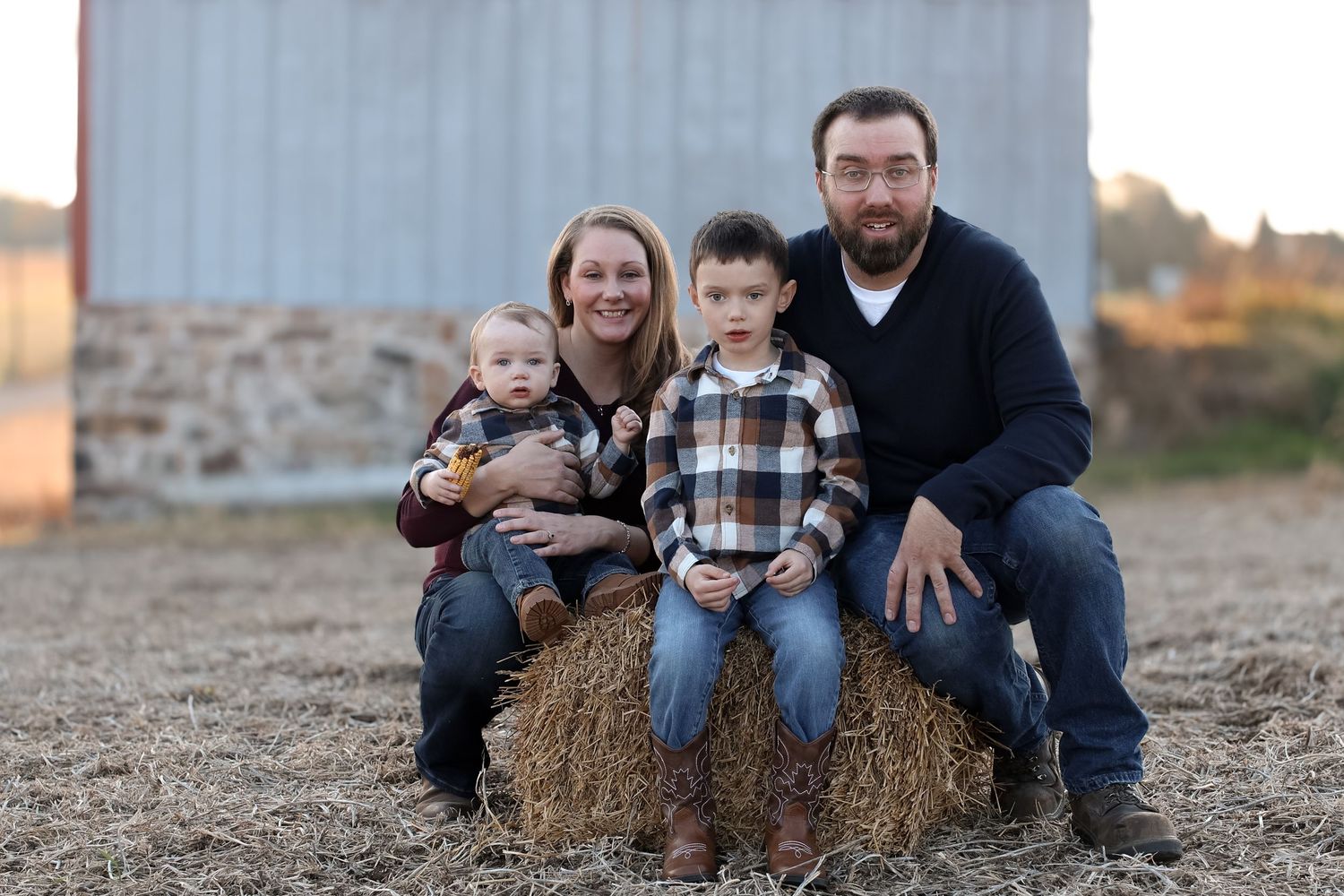 A group sits together on hay bales in a rustic outdoor setting during golden hour.