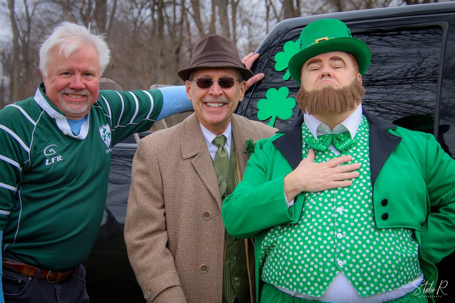 A group of people wearing green clothing and shamrock patterns celebrate St. Patrick's Day festivities outdoors.