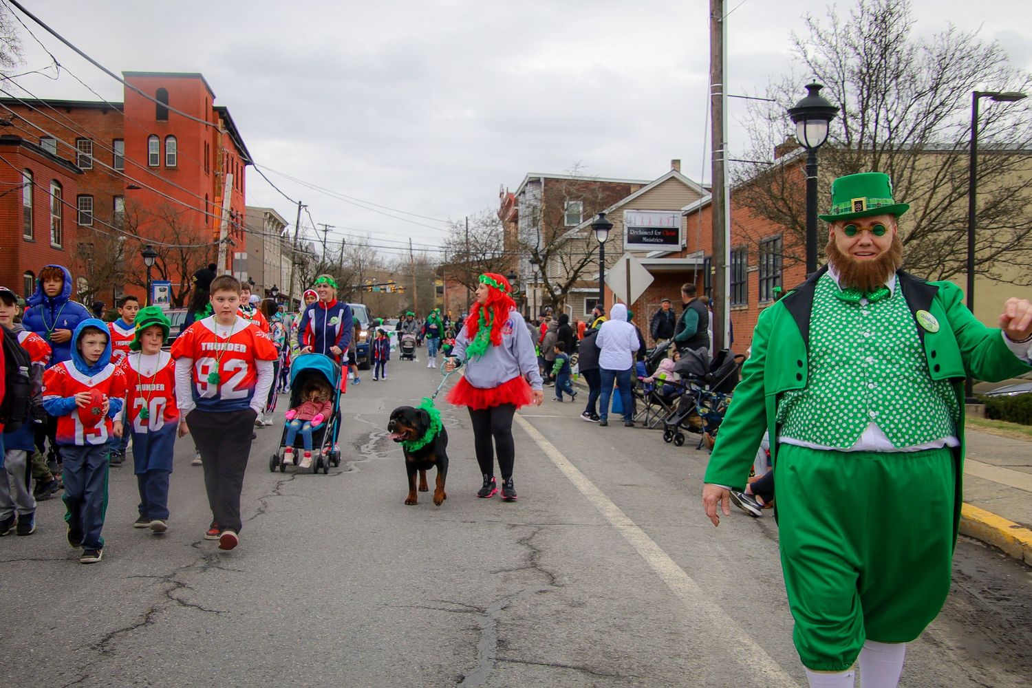 Crowd of people walking in a street parade wearing red and green clothing during a community celebration.