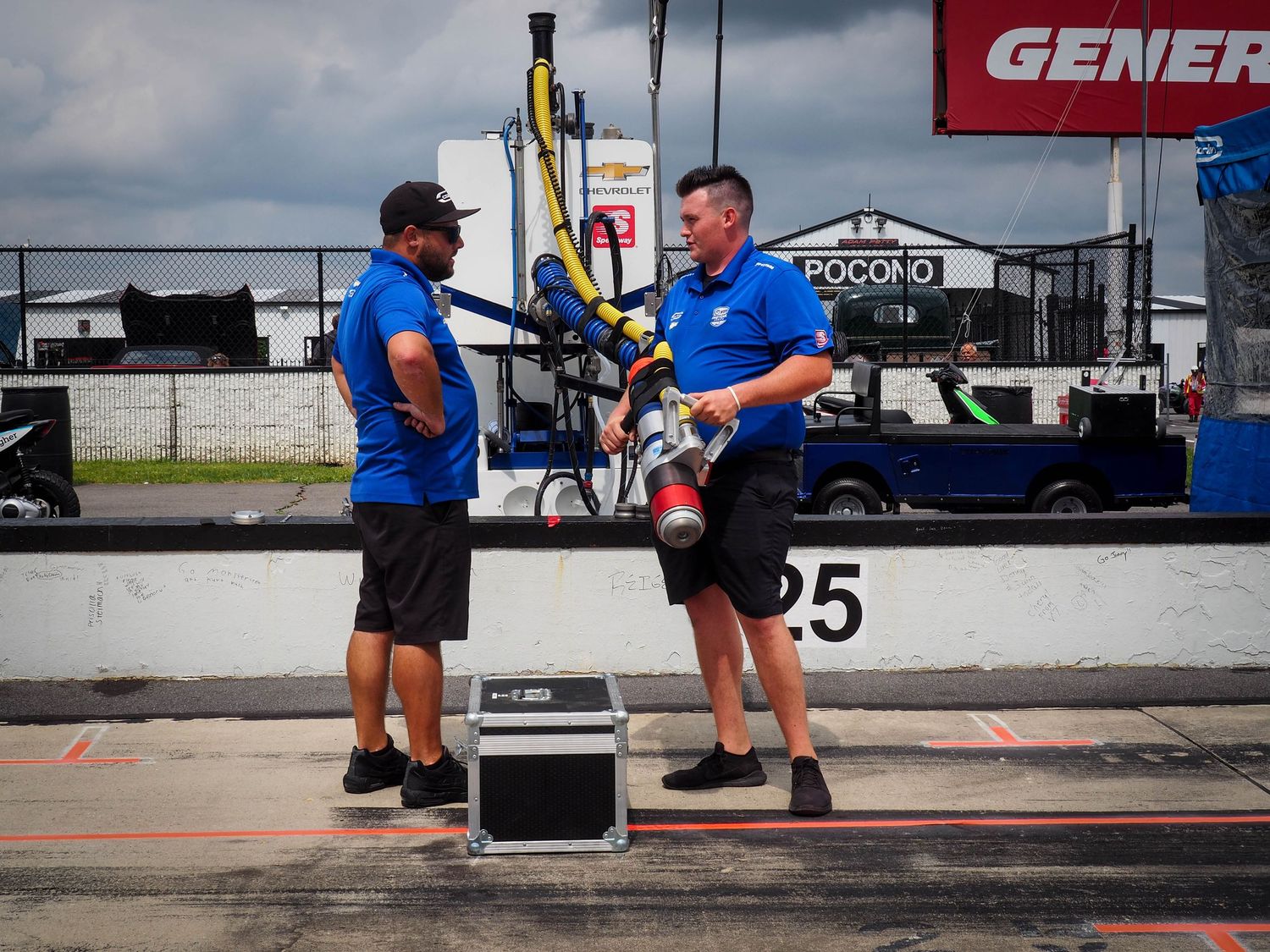 Professional drag racing pit crew members prepare race car equipment in the pit area during a motorsports event.
