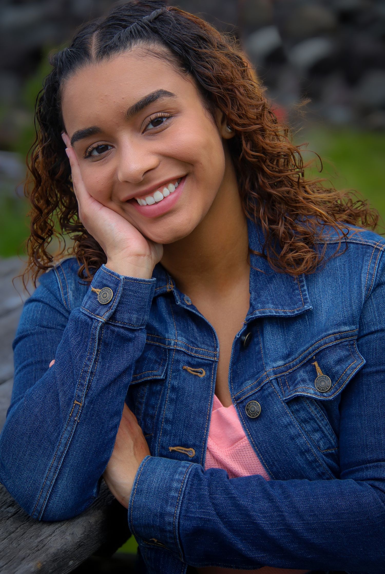 A series of casual portraits showing someone in a denim jacket and pink top posing with natural curly hair outdoors.