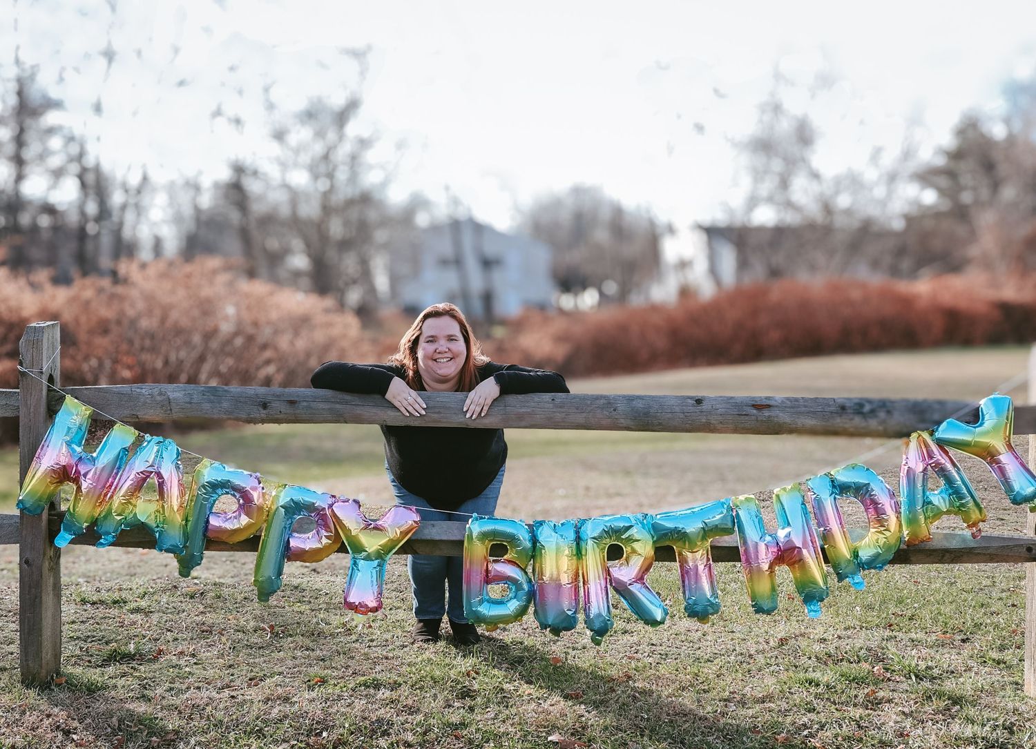 A colorful birthday banner with bright letters hangs between two trees in an outdoor setting.