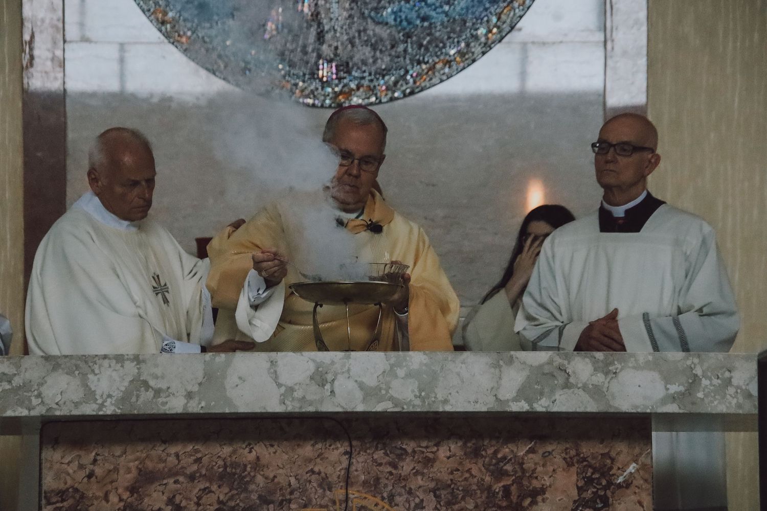 Several people in white robes gather around a table for a ceremonial meal or religious service.