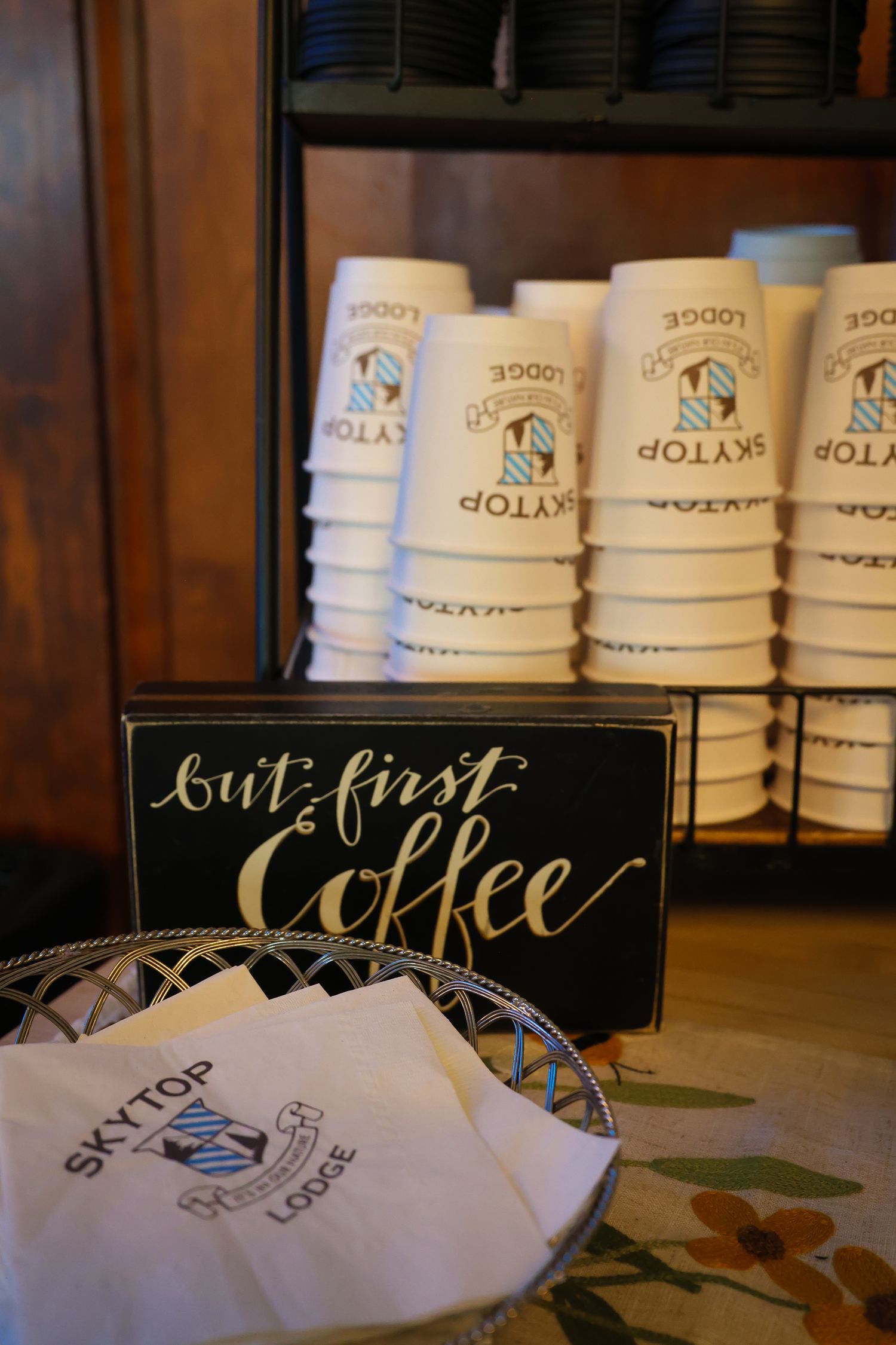 Coffee shop counter displays stacked white cups and black signage with elegant lettering in warm lighting.