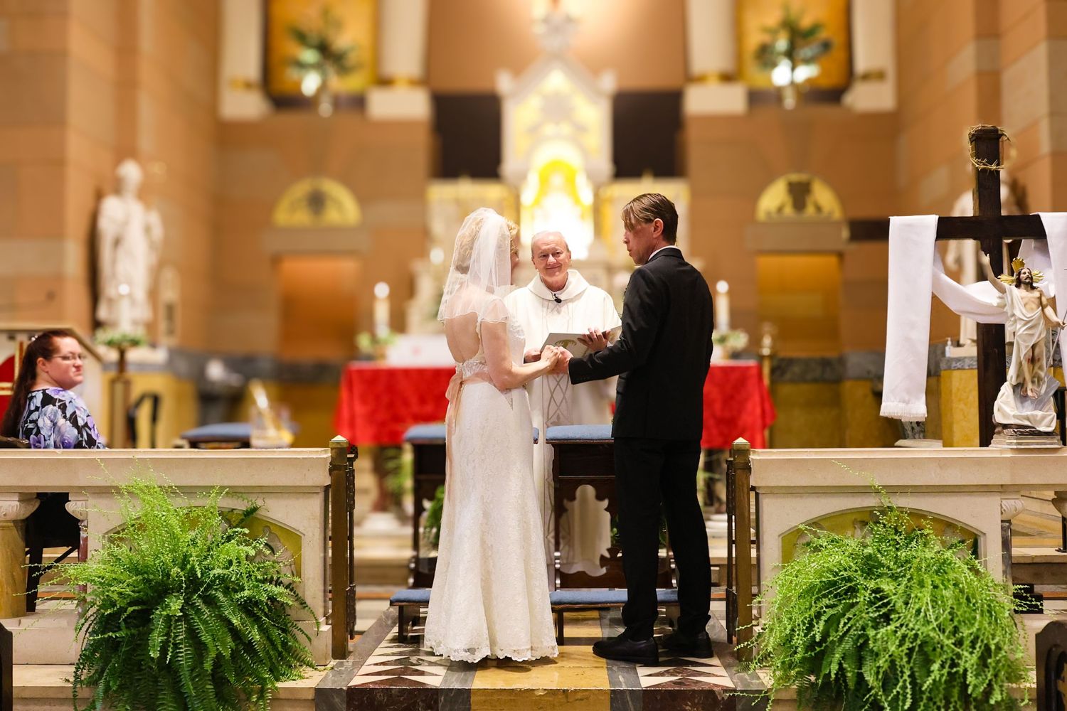 A couple exchanges vows during a traditional church wedding ceremony with potted ferns decorating the altar steps.