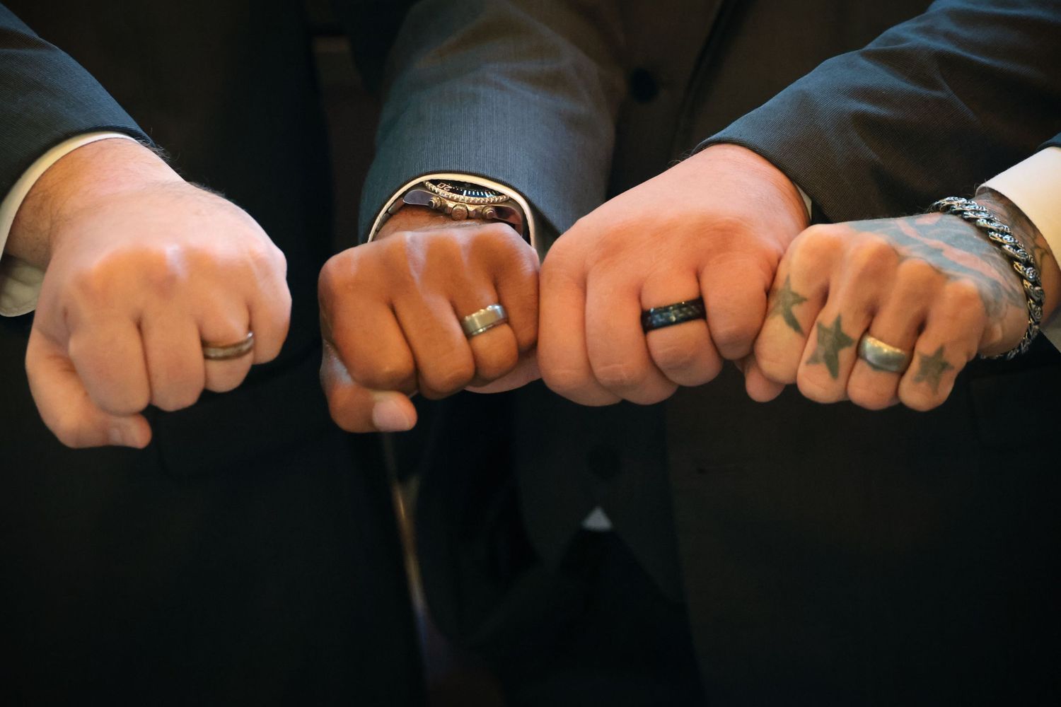 Four hands lined up showing off matching black wedding rings against dark clothing.