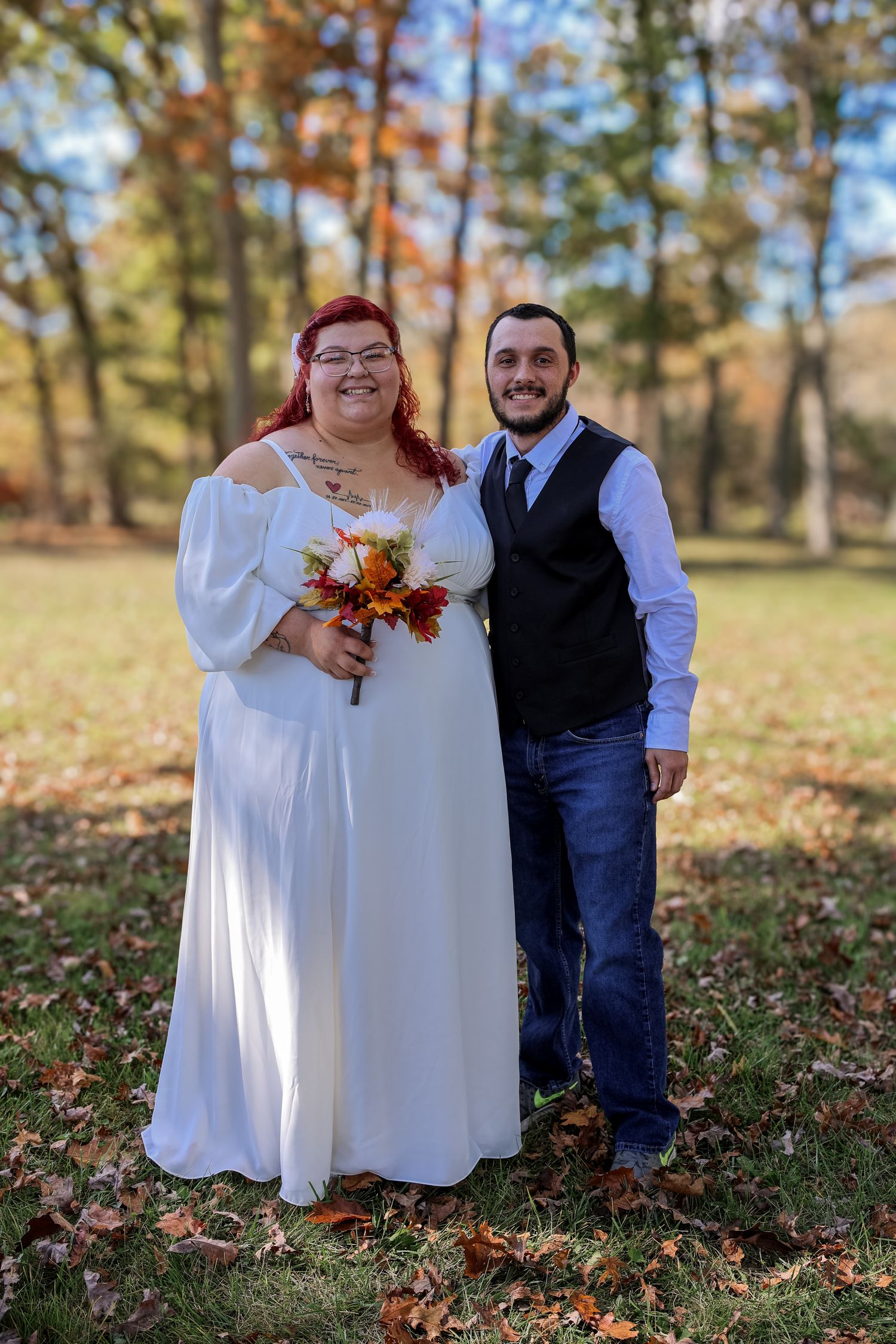 Autumn wedding couple poses together in a wooded area with fallen leaves and natural light filtering through trees.