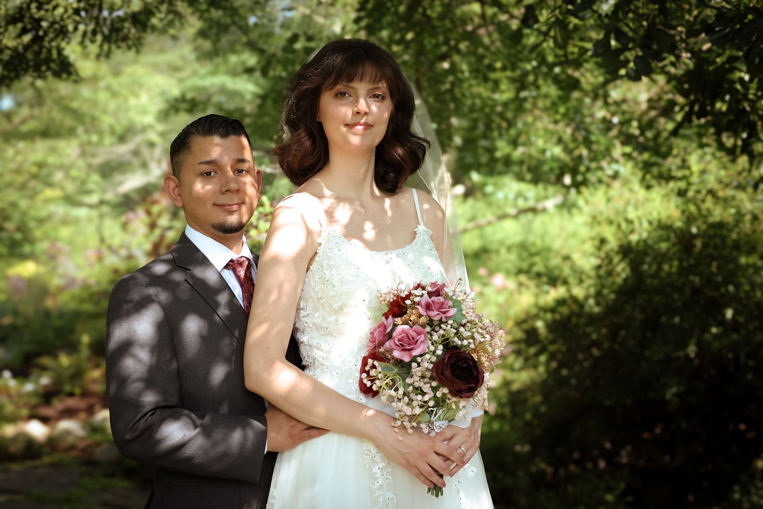 A bride and groom pose together in a garden setting during their outdoor wedding celebration.