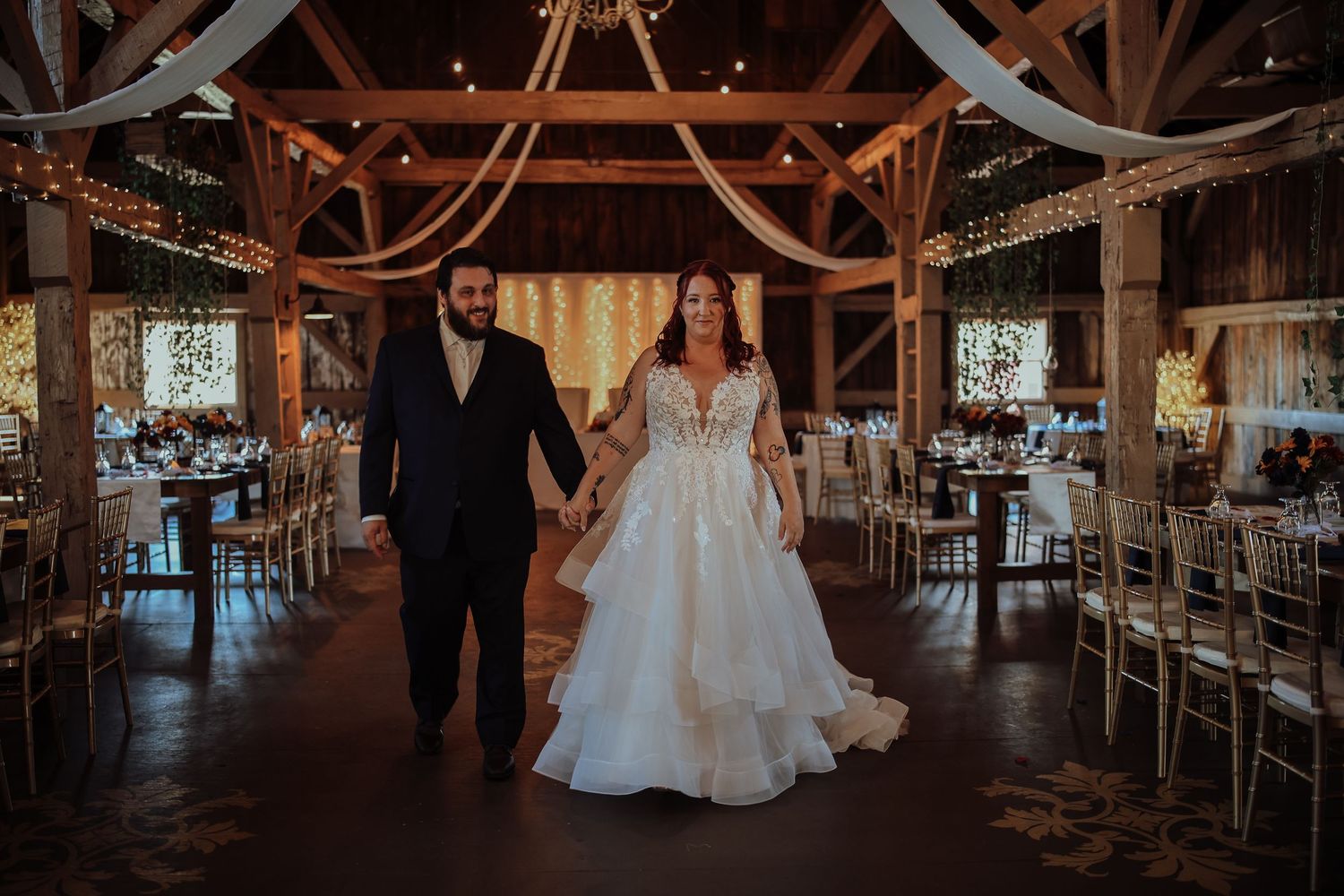 Couple dancing together in a rustic barn venue with romantic lighting and wooden beams overhead.