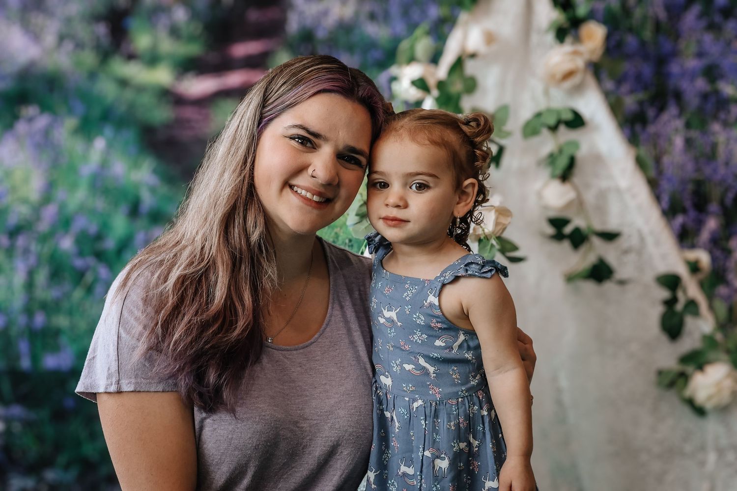 Mother and daughter share joyful moments together in a garden setting with purple flowers in the background.