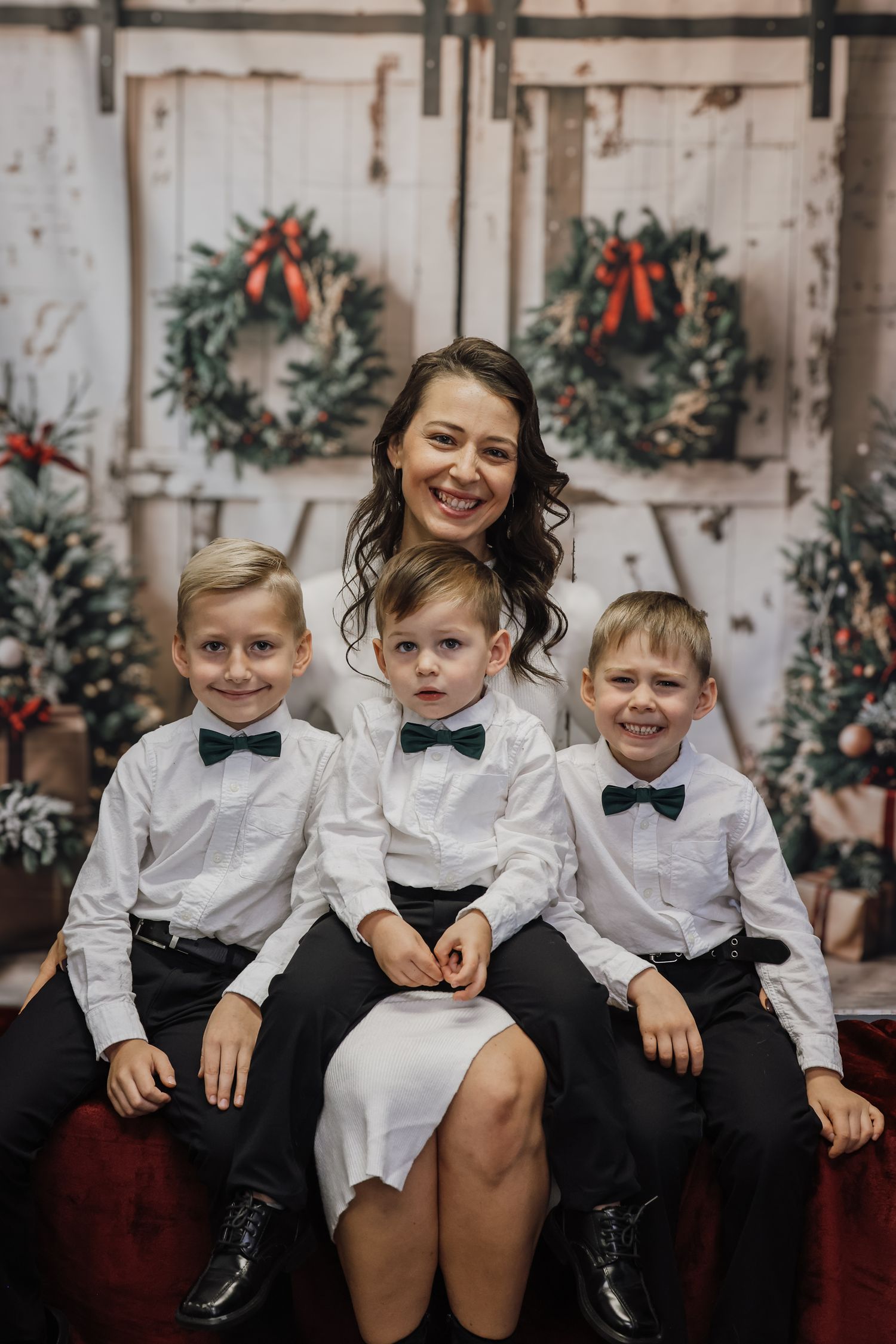 A smiling woman poses with three boys in matching white shirts and black bow ties for a festive Christmas photo.