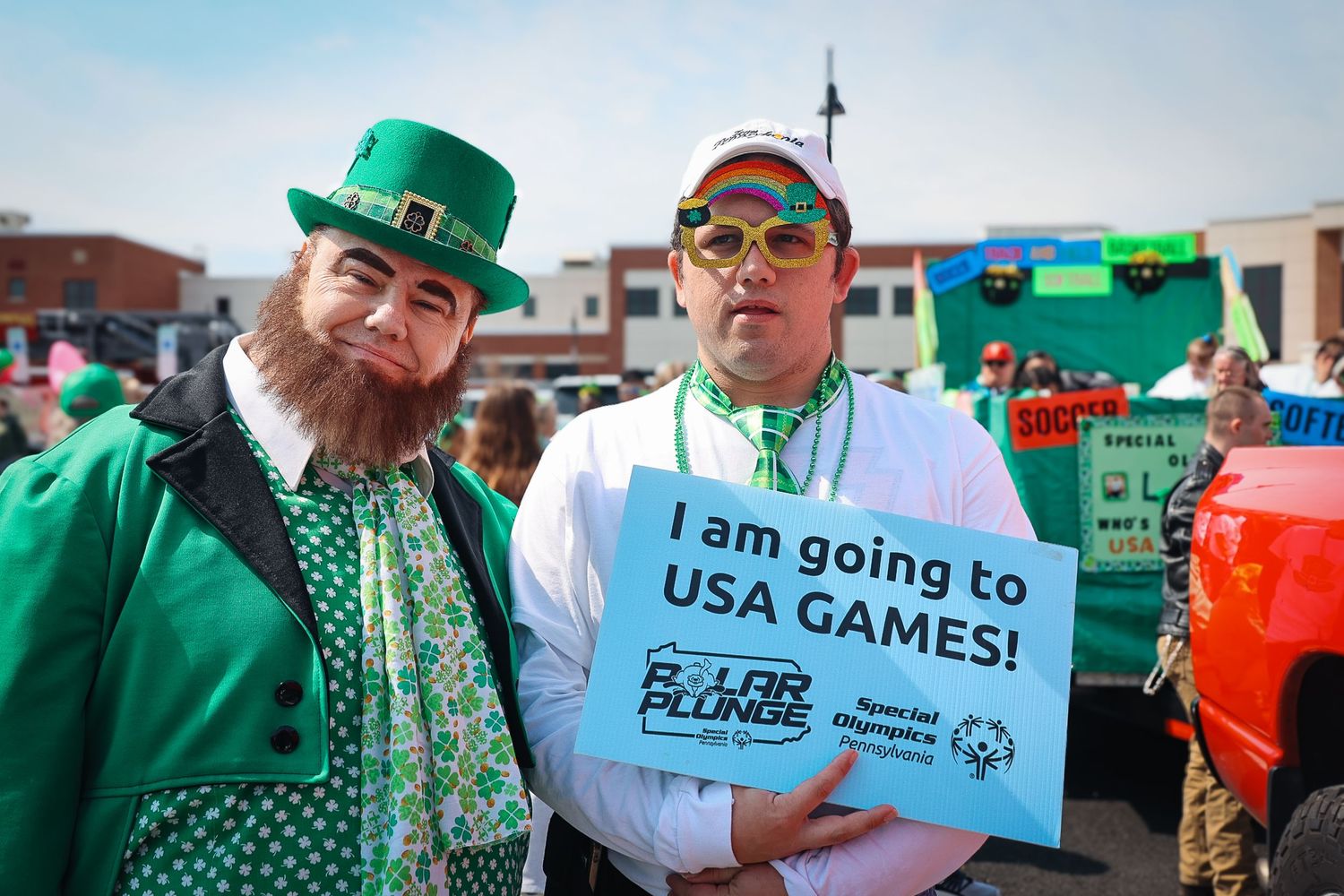 Two men in St. Patrick's Day costumes, one holding a sign reading I am going to USA Games at a Polar Plunge event.