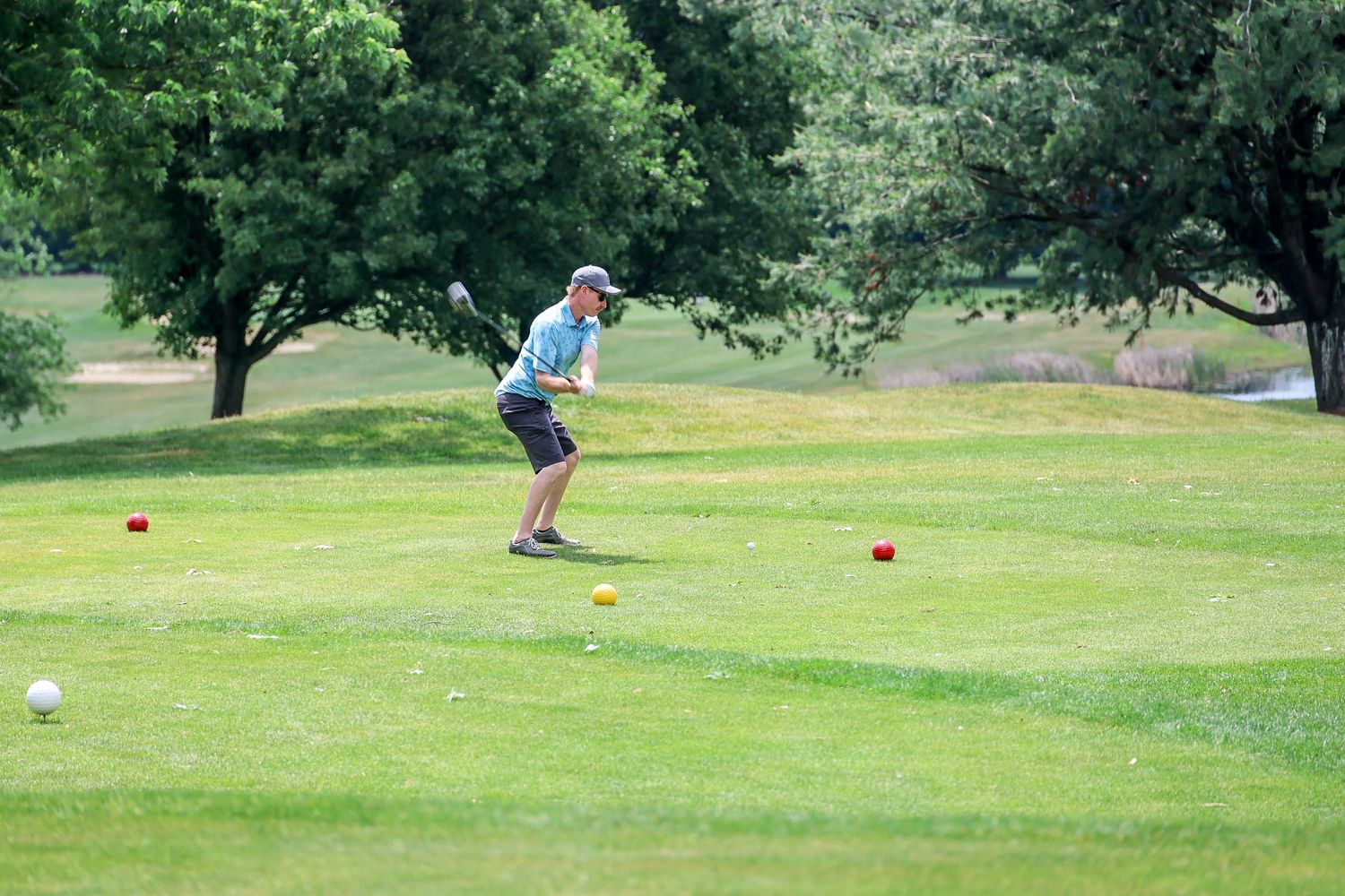 Golfer follows through on a swing on a sunny green golf course with colorful tee markers.