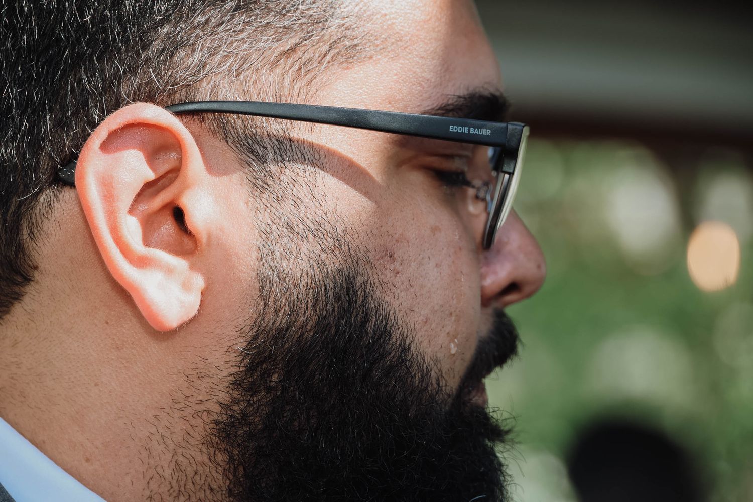 Close-up profile of a bearded man wearing black-framed glasses at an outdoor event.