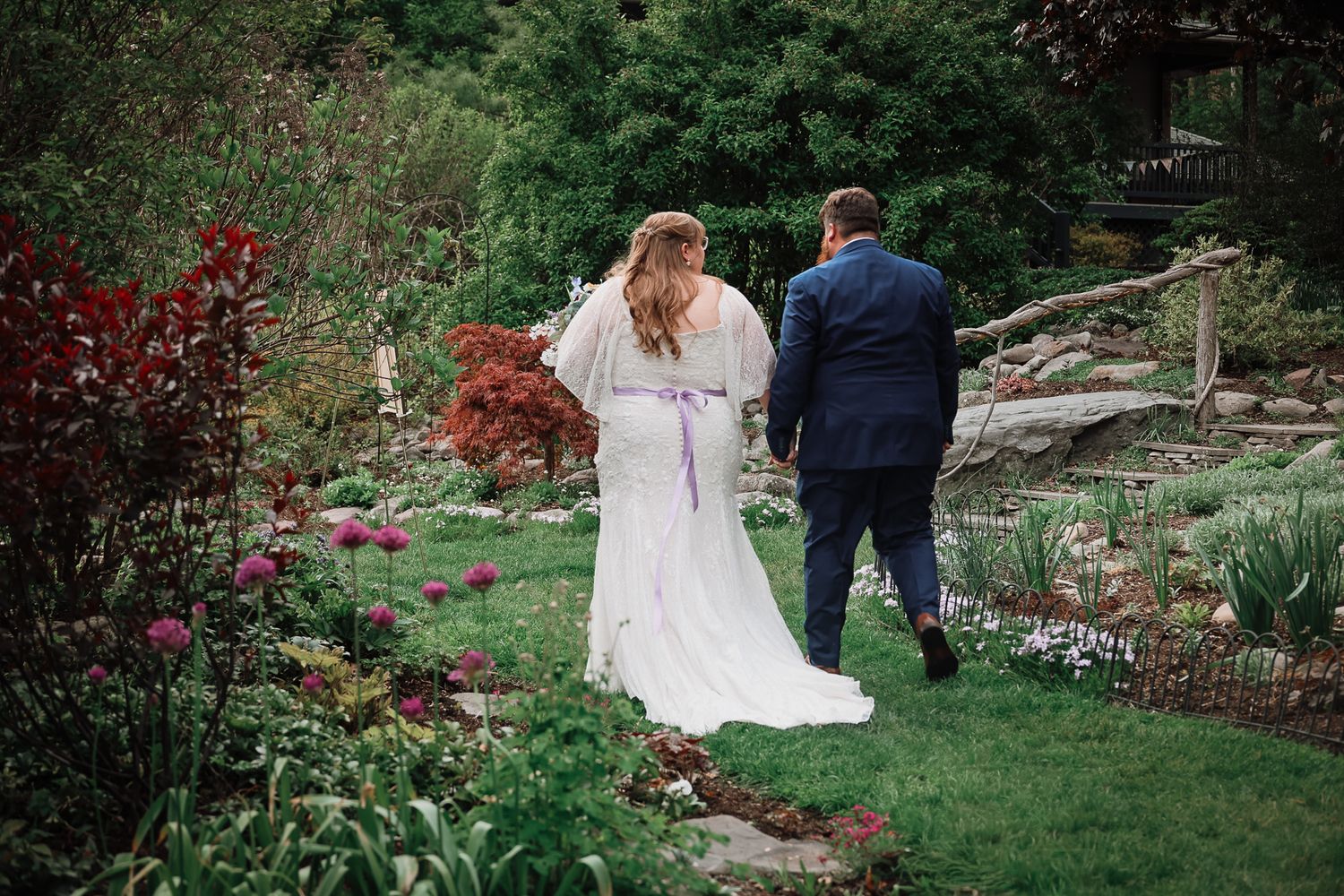 Bride and groom walking hand in hand through a lush garden wedding venue with colorful flowers.