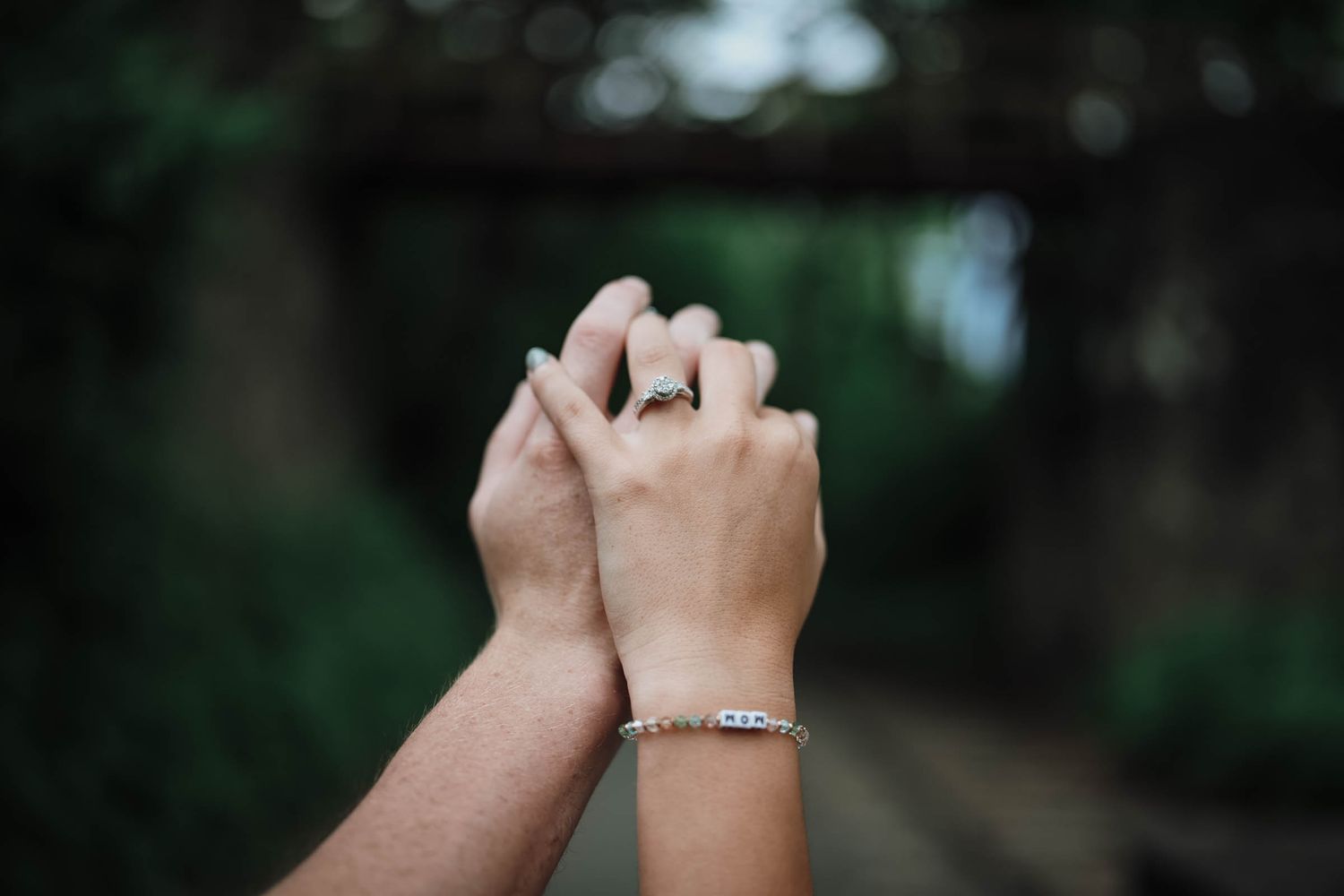 Close-up of couple holding hands with engagement ring and bracelet visible outdoors.