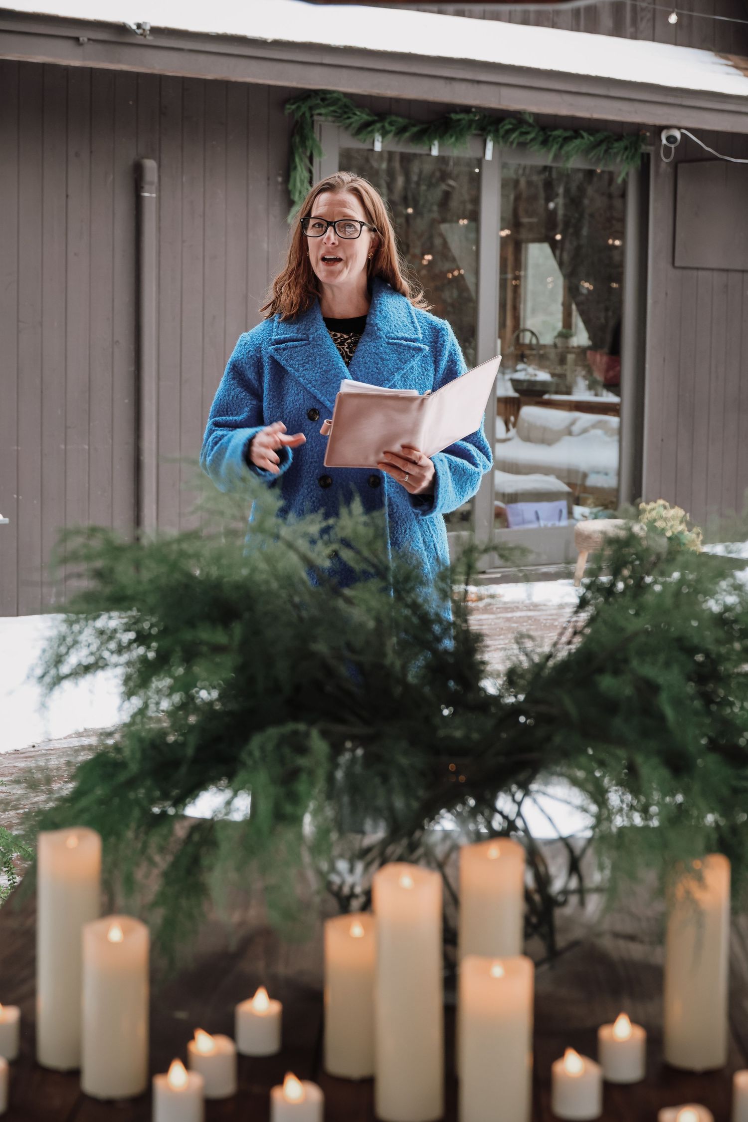 A row of glowing white pillar candles arranged beneath evergreen branches creates an elegant holiday atmosphere.