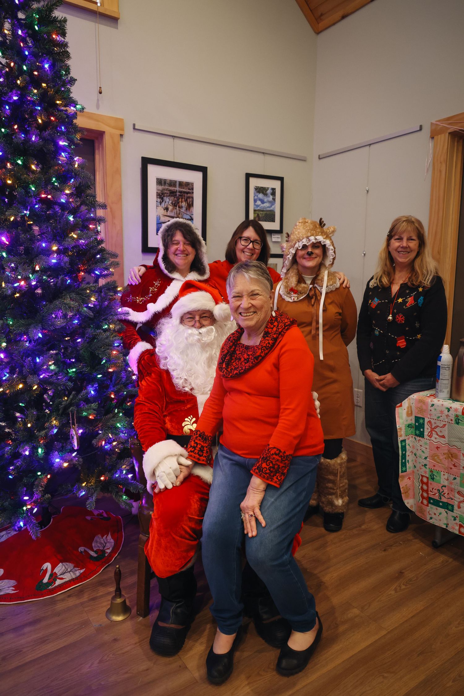 A festive Christmas scene with a decorated purple-lit tree and holiday gathering in a community room.