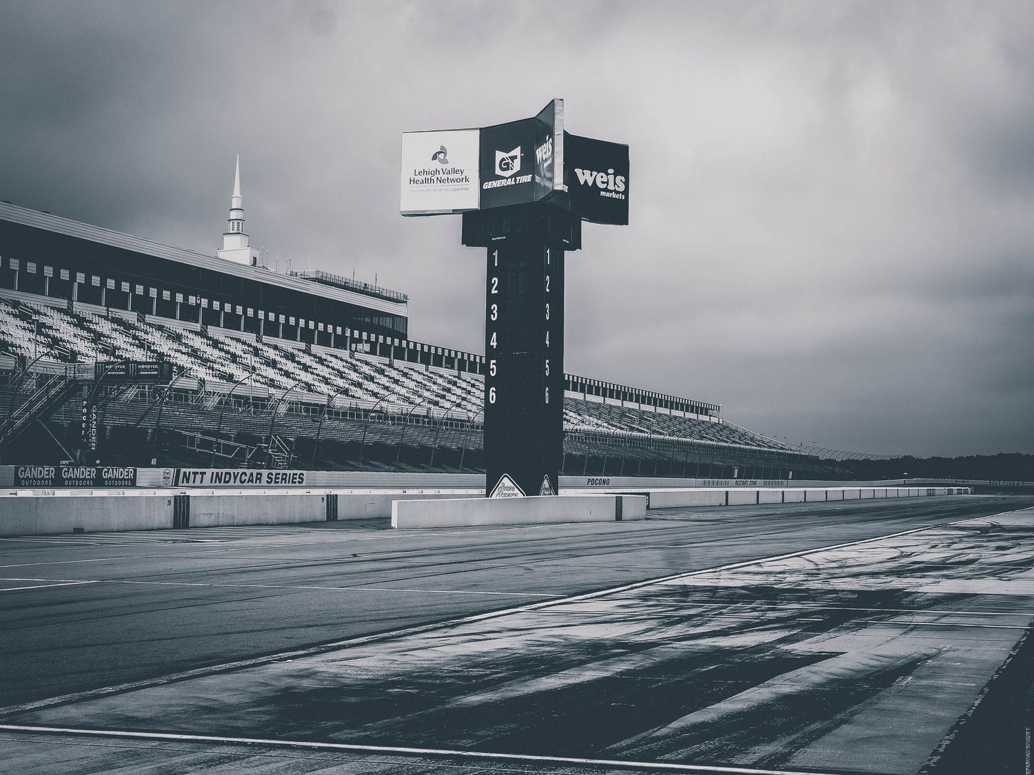 A dramatic view of an empty racetrack grandstand under moody gray skies with repeating geometric patterns.