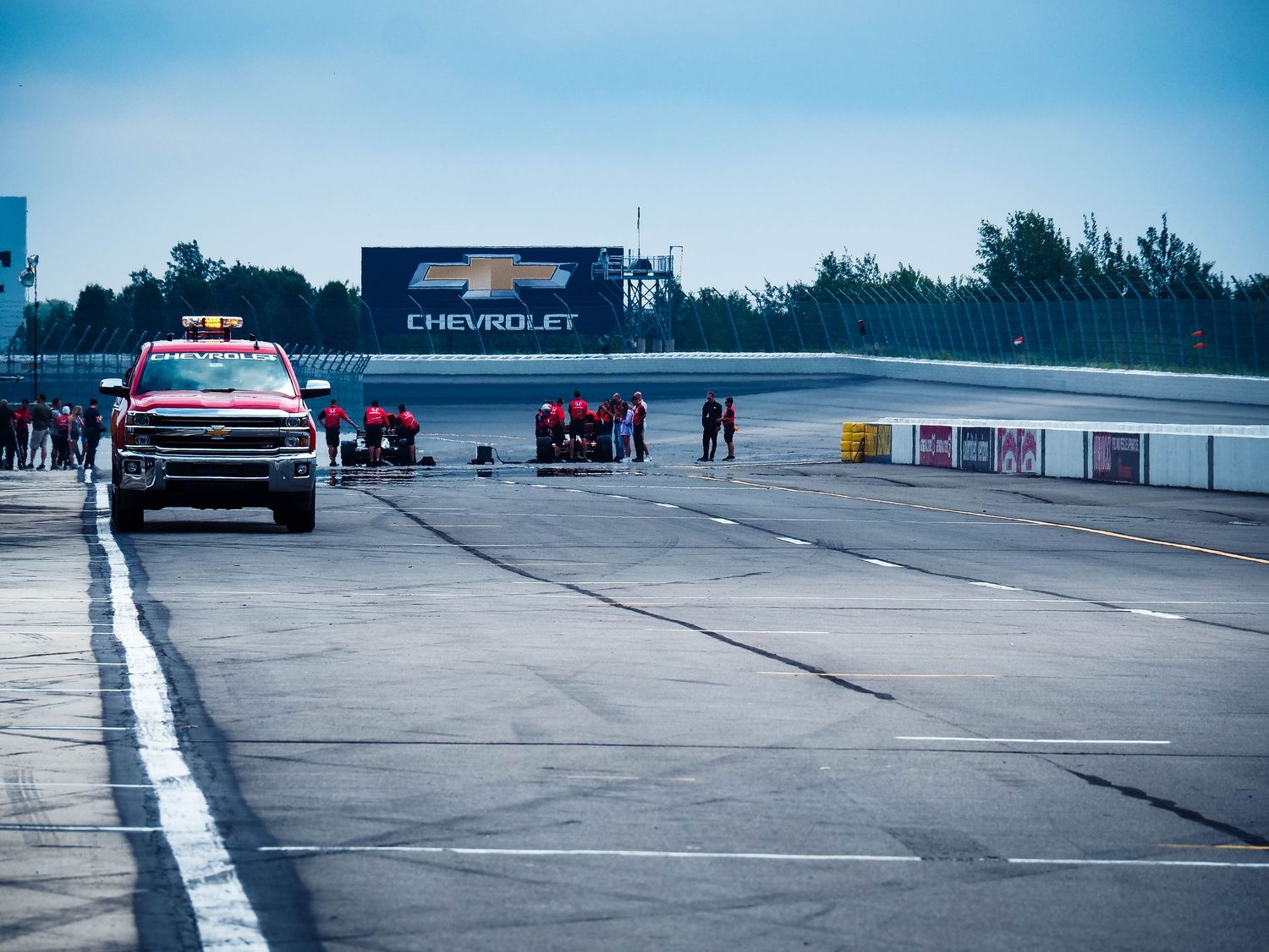 Race track pit lane with Chevrolet signage and vehicles lined up during a motorsport event at dusk.