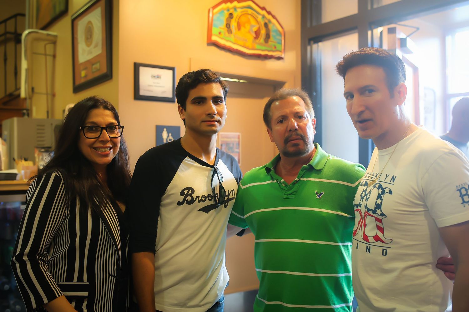 A group of four people standing together and smiling inside a casual restaurant or bar setting.