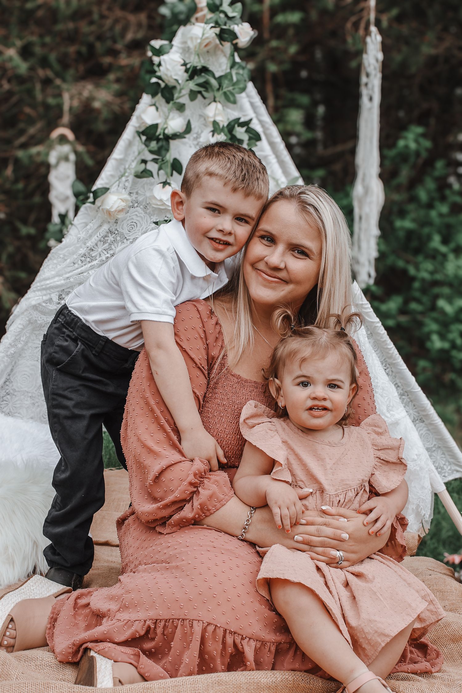 Family portrait session in outdoor setting with decorative white teepee and greenery backdrop.