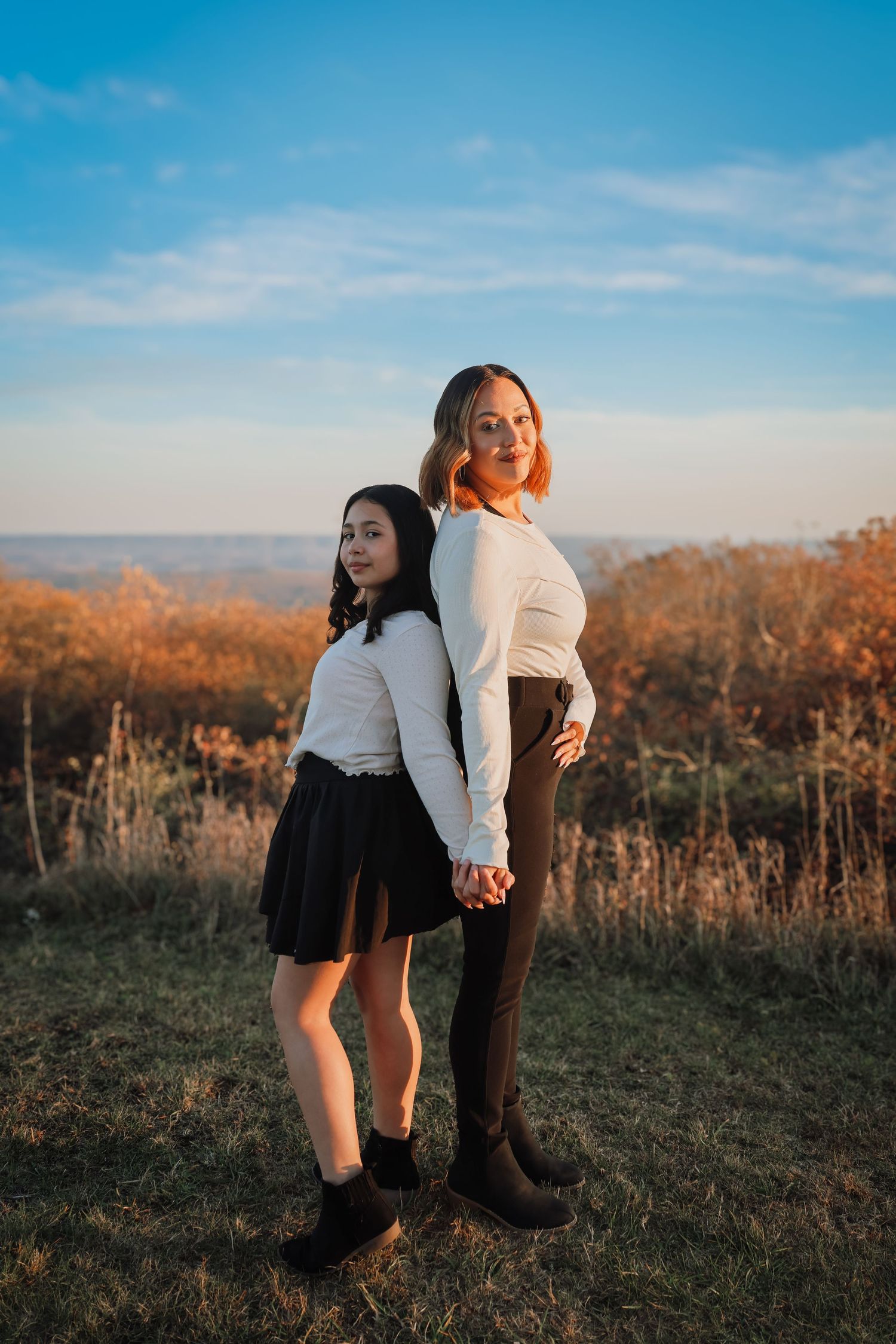 A couple embraces in a romantic pose against a scenic autumn hilltop during golden hour sunset.