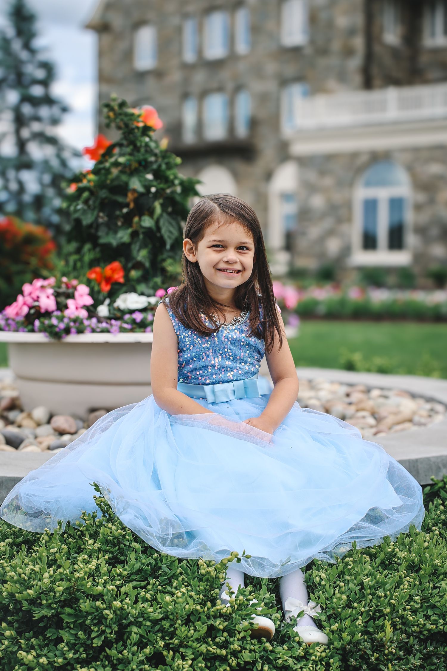 A series of photos showing a light blue tulle dress against green bushes and stone architecture in the background.