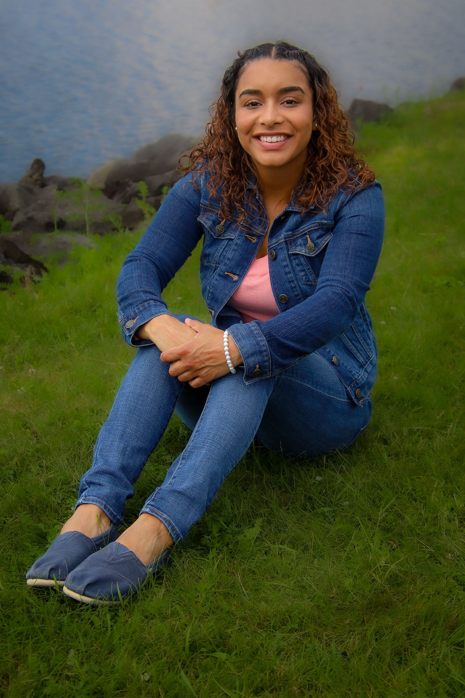 Someone in double denim lounges on grassy hillside with ocean view in casual outdoor photoshoot series.