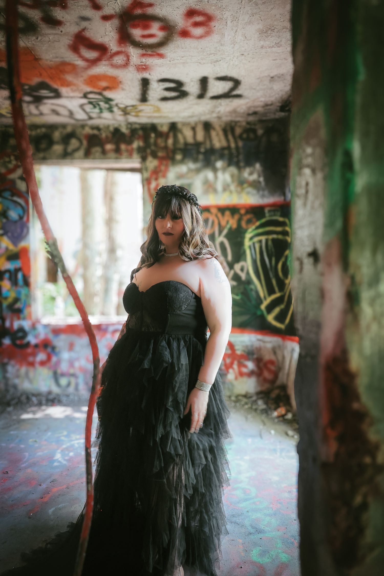 A person in a black tulle dress poses in an abandoned building covered with graffiti art and colorful tags.