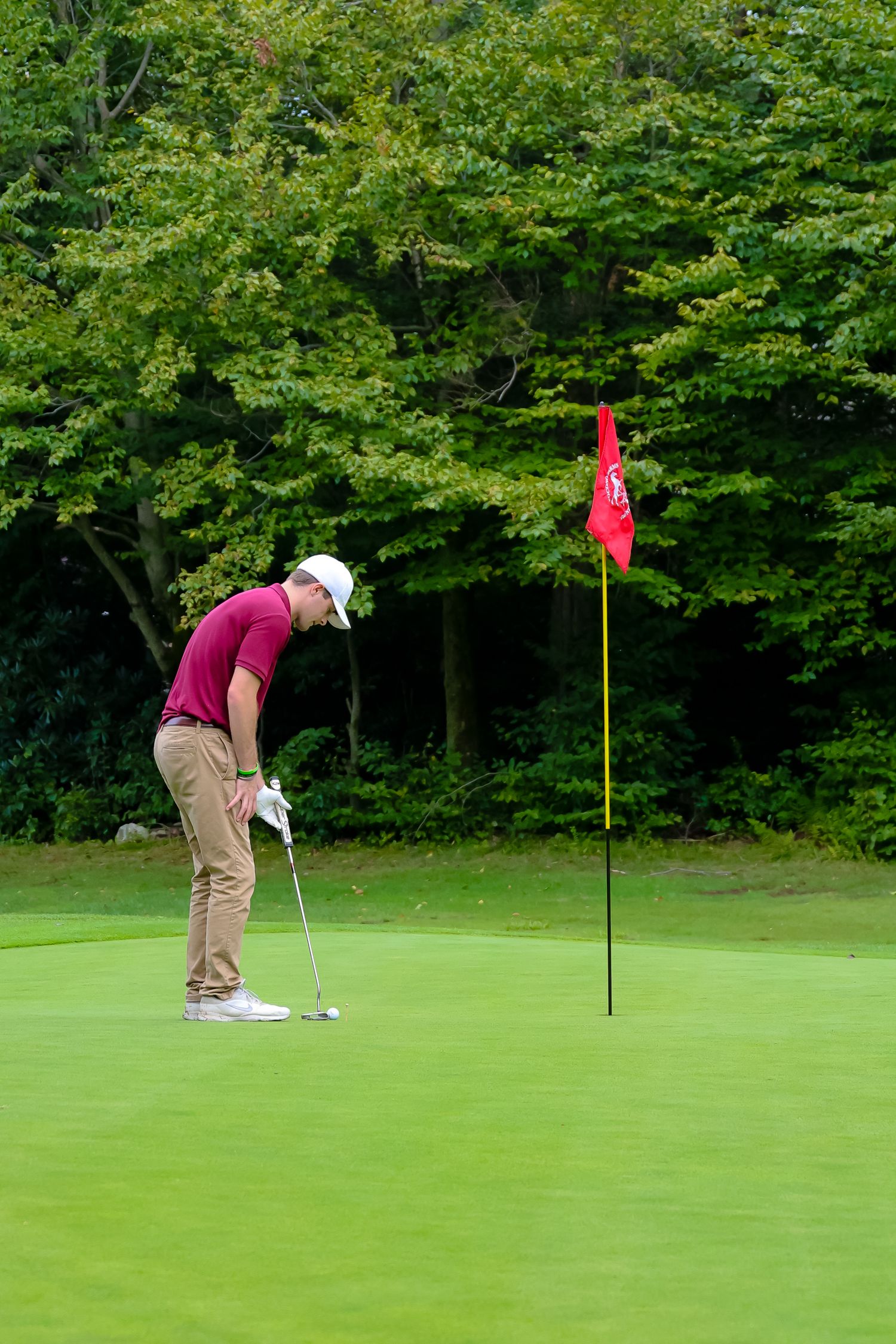 A golfer lines up and putts on a lush green golf course with a red flag pin in the background.