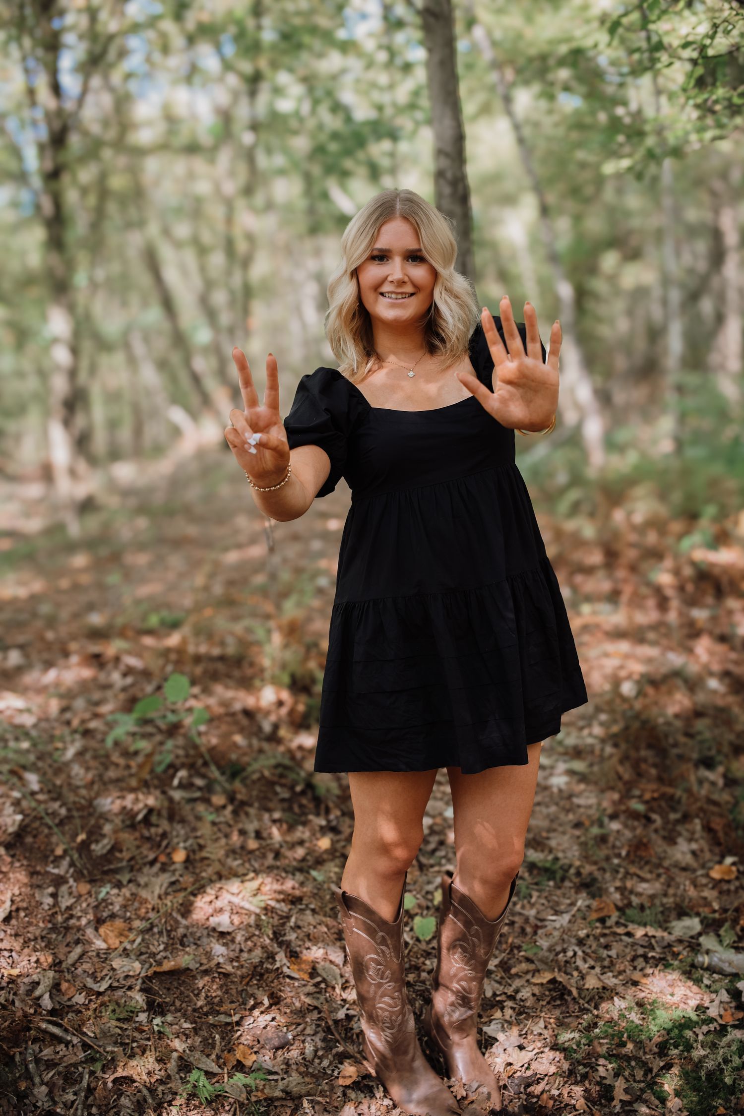 A series of playful outdoor portraits showing someone in a black dress making hand gestures against a wooded backdrop.