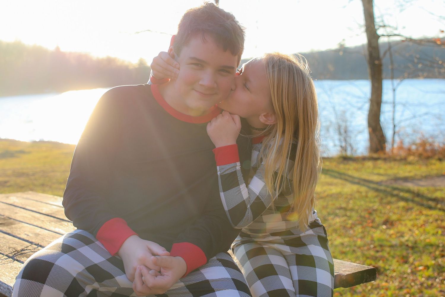 A couple shares a tender moment on a wooden bench by a lake during golden hour sunset.